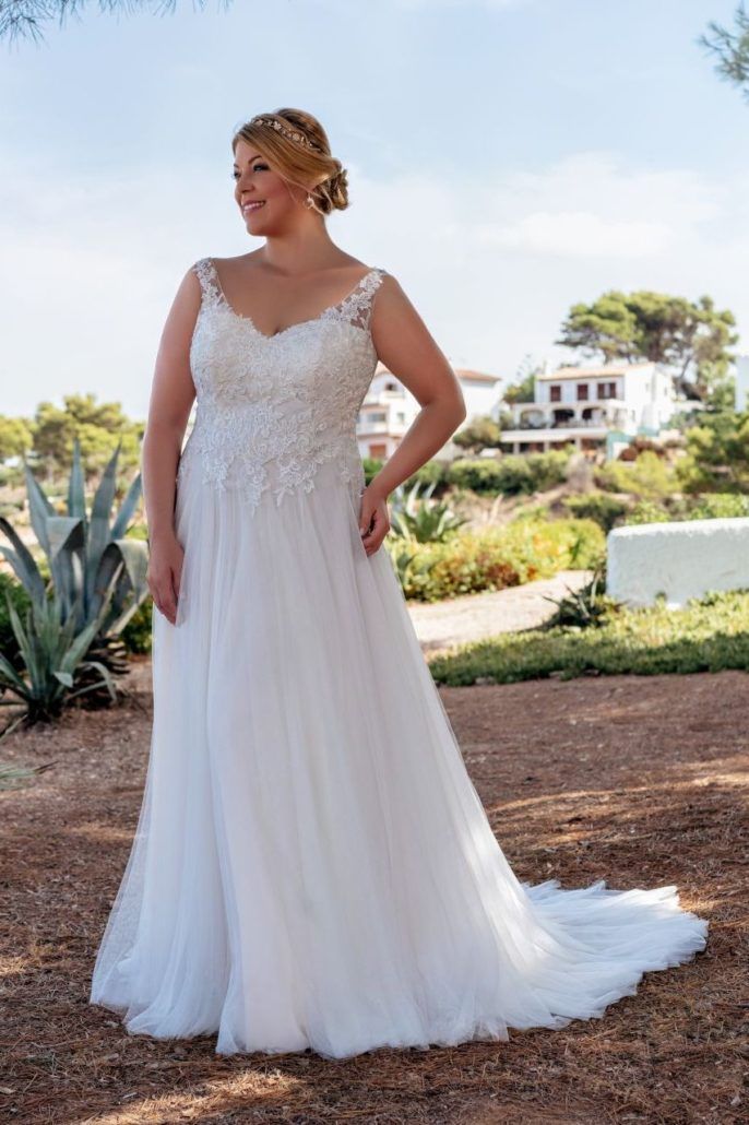 Eine Übergrößenbraut in einem weißen Brautkleid steht in einem Park.