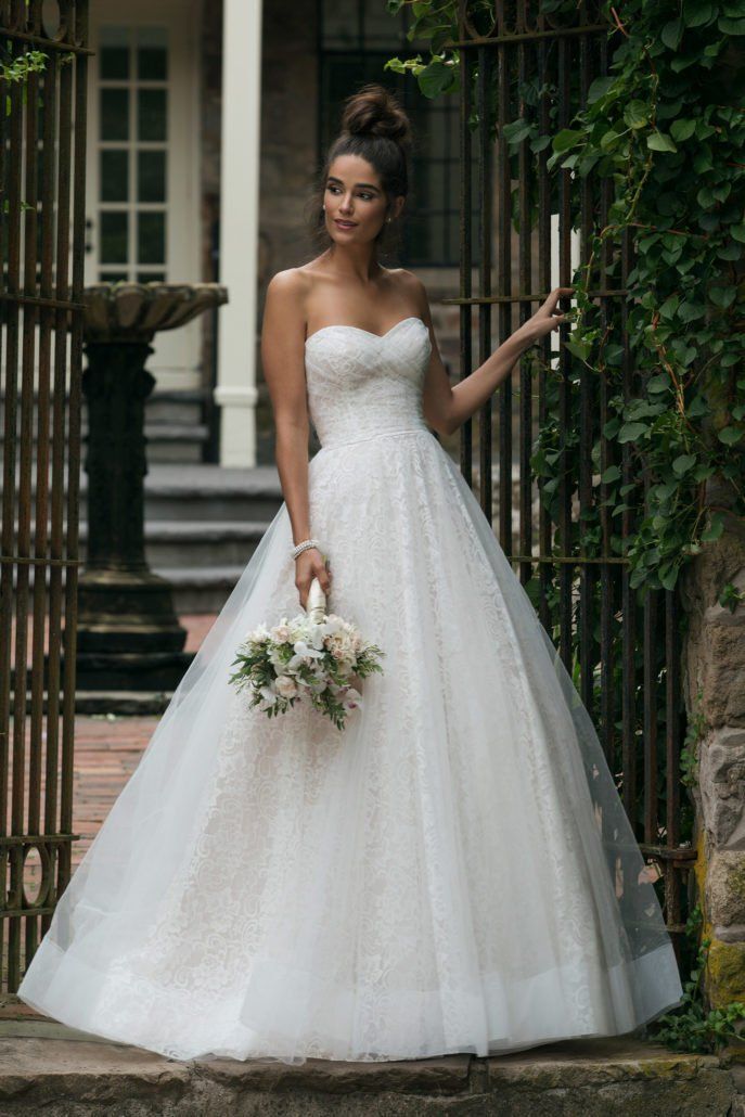 Eine Frau in einem weißen Hochzeitskleid hält einen Blumenstrauß.