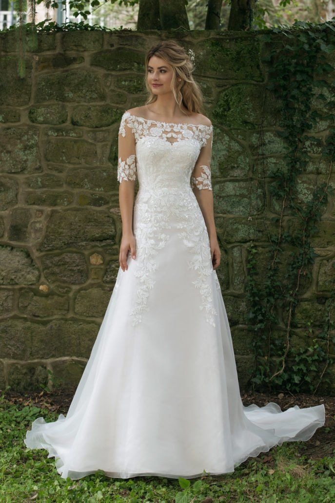 Eine Frau in einem weißen Hochzeitskleid steht vor einer Steinmauer.