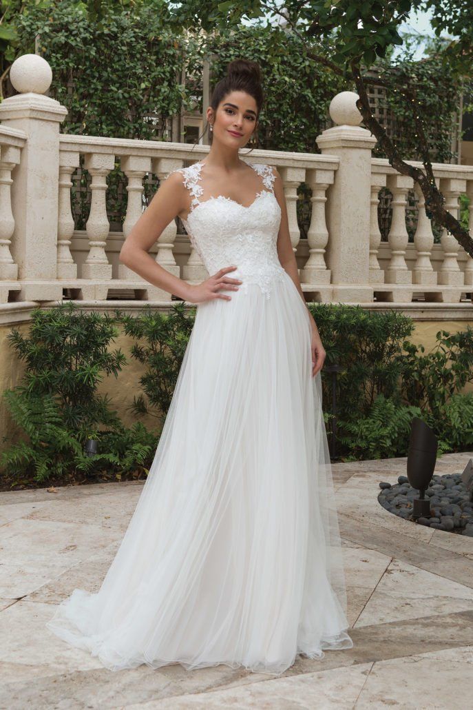 Eine Frau in einem weißen Brautkleid steht vor einem Zaun.
