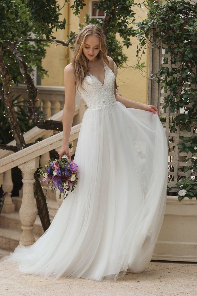 Eine Frau in einem weißen Hochzeitskleid hält einen Blumenstrauß.