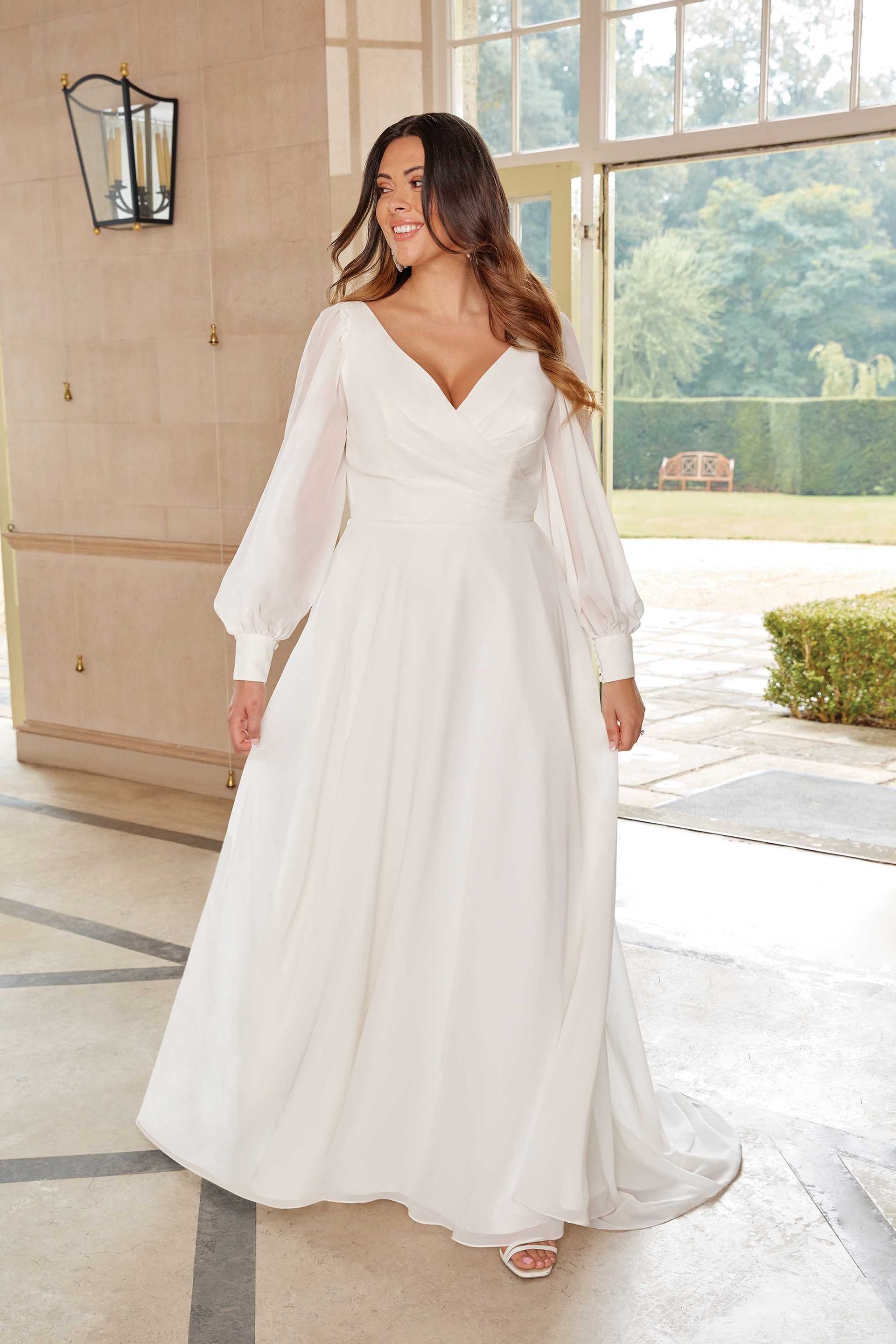 Eine Frau trägt ein weißes Hochzeitskleid mit langen Ärmeln.