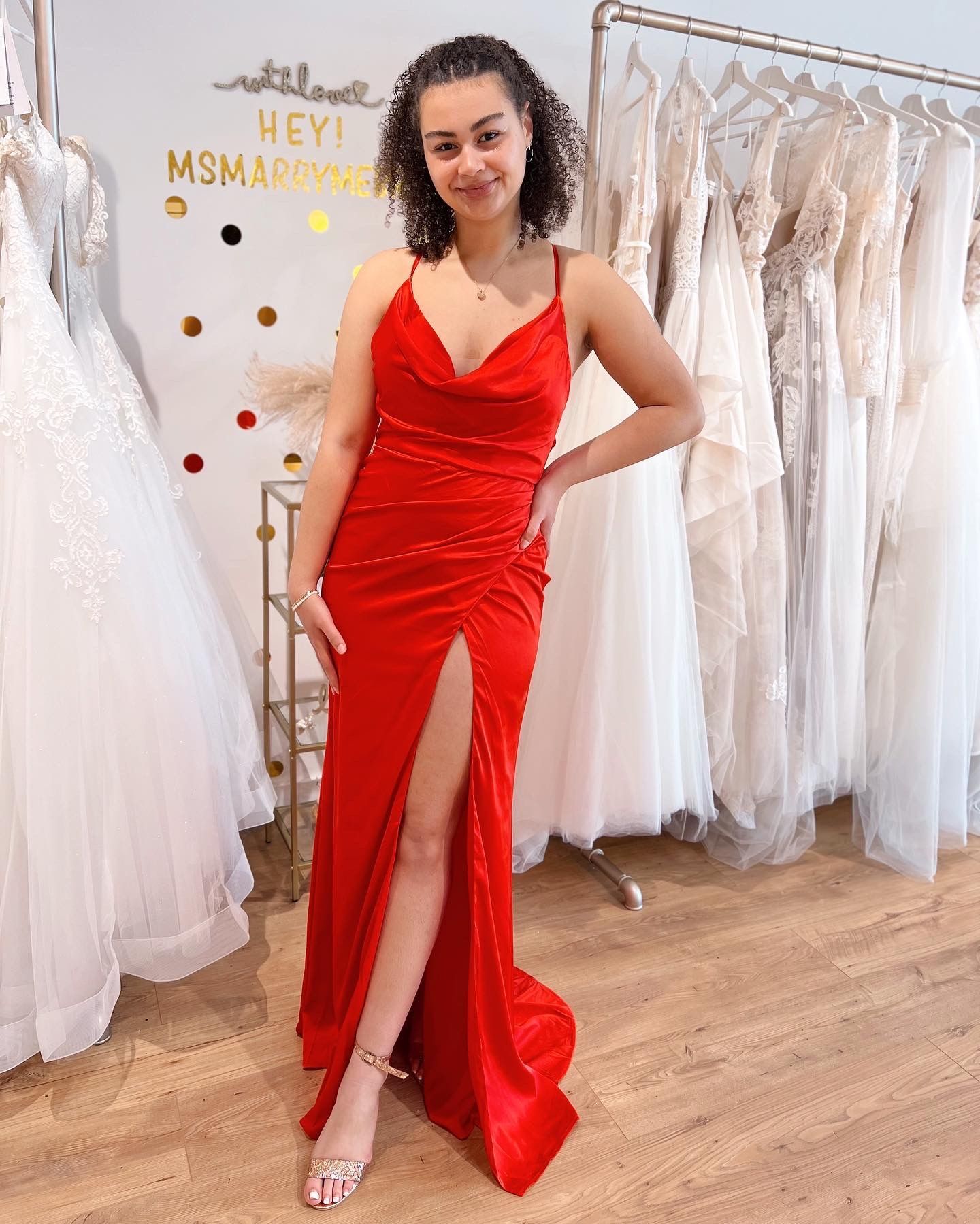 Eine Frau in einem roten Kleid steht vor einem Ständer mit Brautkleidern.