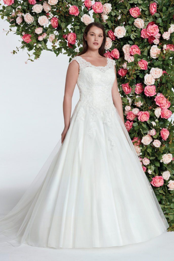 Eine Frau in einem weißen Hochzeitskleid steht vor einer Wand aus rosa Rosen.