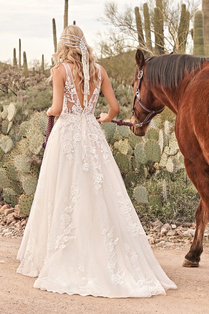Eine Frau in einem Hochzeitskleid steht neben einem Pferd in der Wüste.