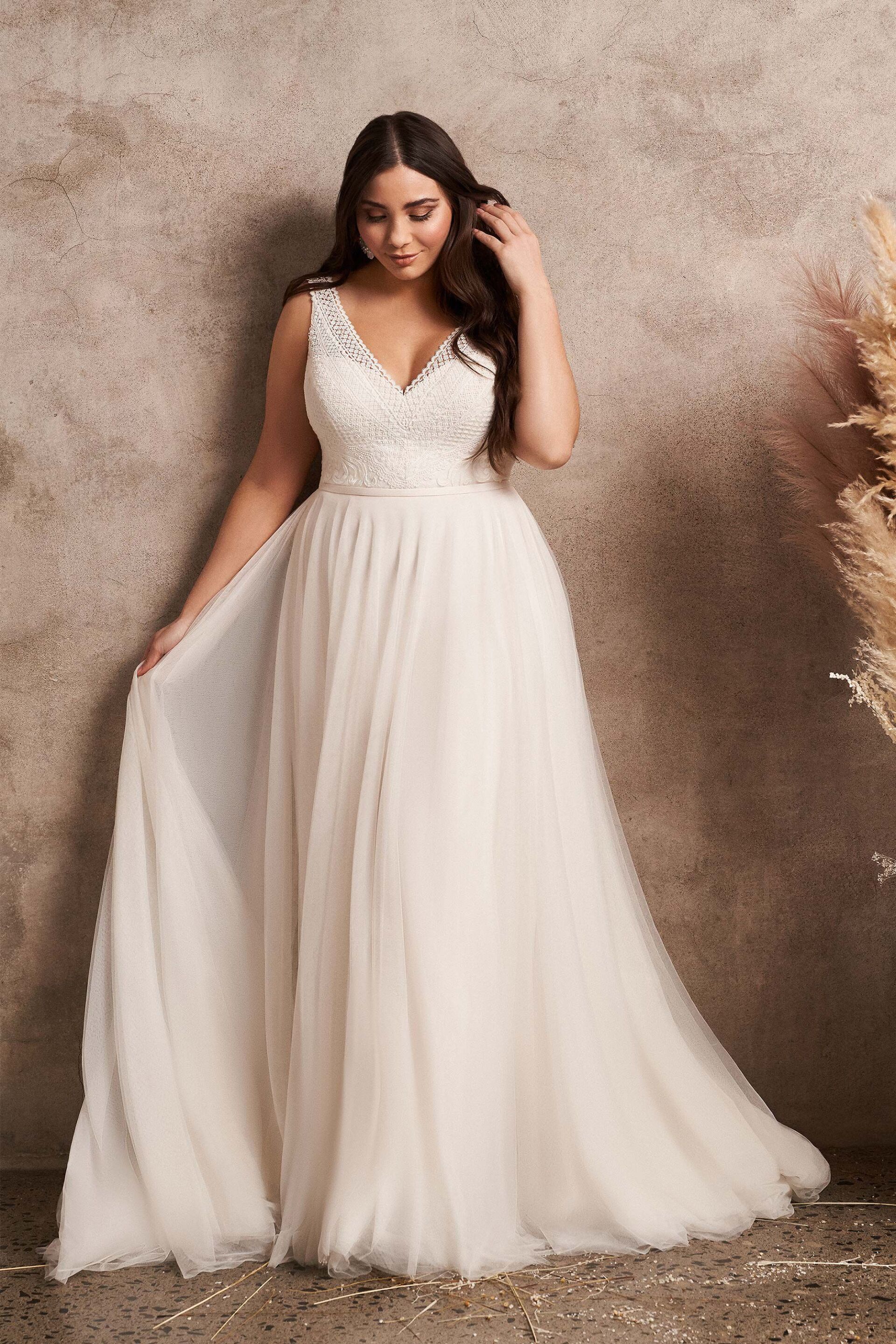 Eine Frau in einem weißen Brautkleid steht vor einer Wand.