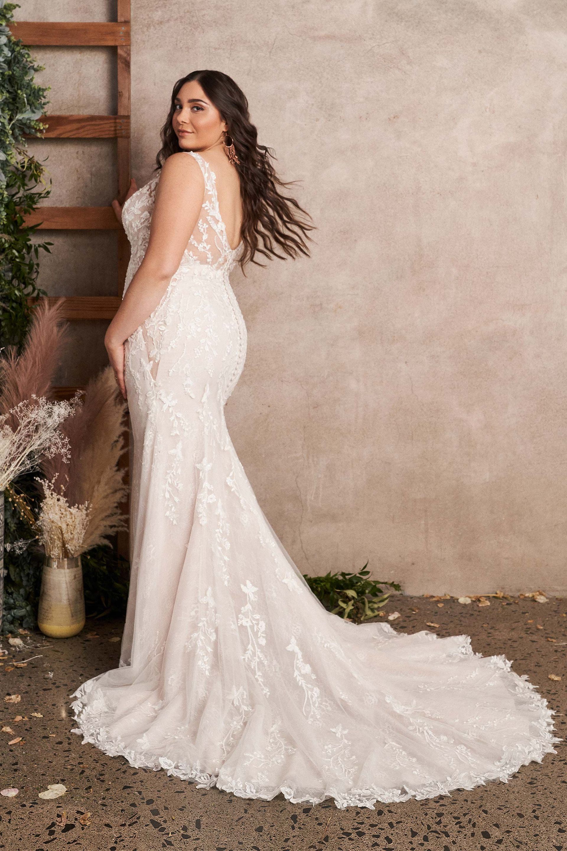 Eine Übergrößenbraut in einem Brautkleid steht vor einer Wand.