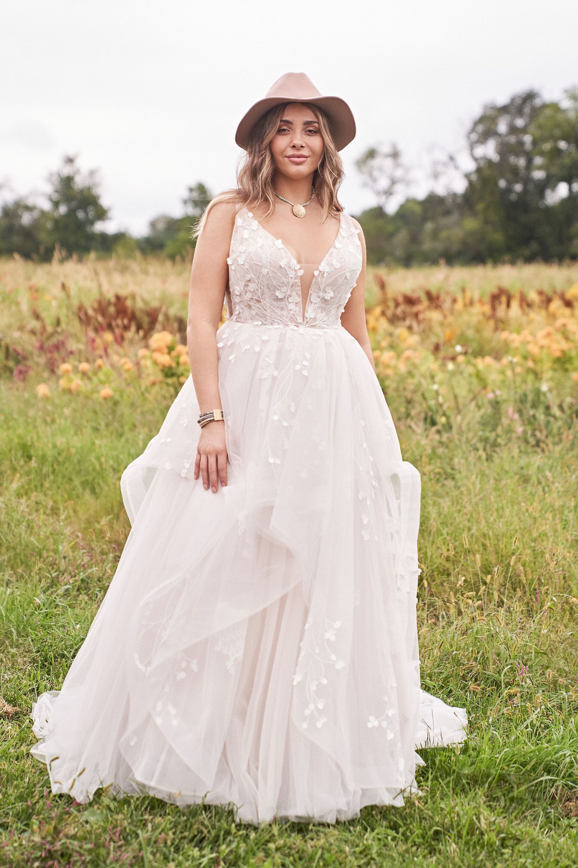 Eine Frau in einem Hochzeitskleid und Hut steht auf einem Feld.