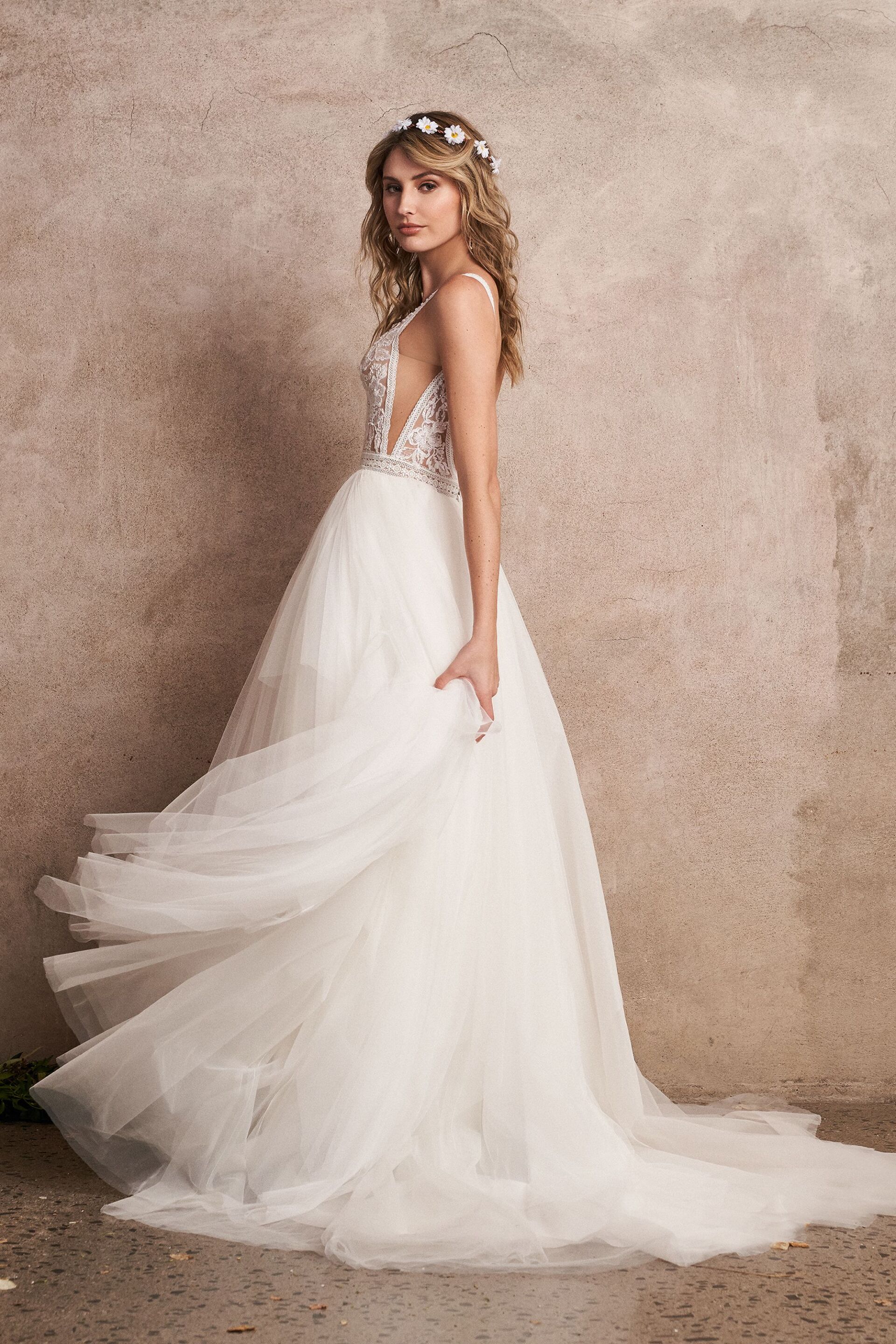 Eine Frau in einem weißen Brautkleid steht vor einer Wand.