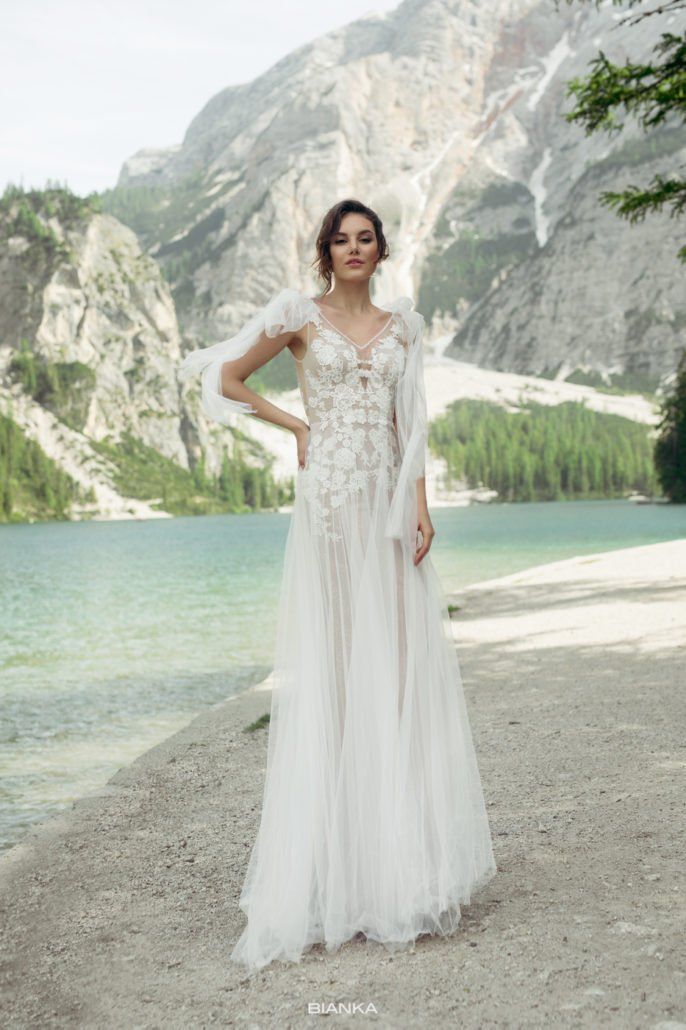 Eine Frau in einem Brautkleid steht an einem Strand in der Nähe eines Sees.