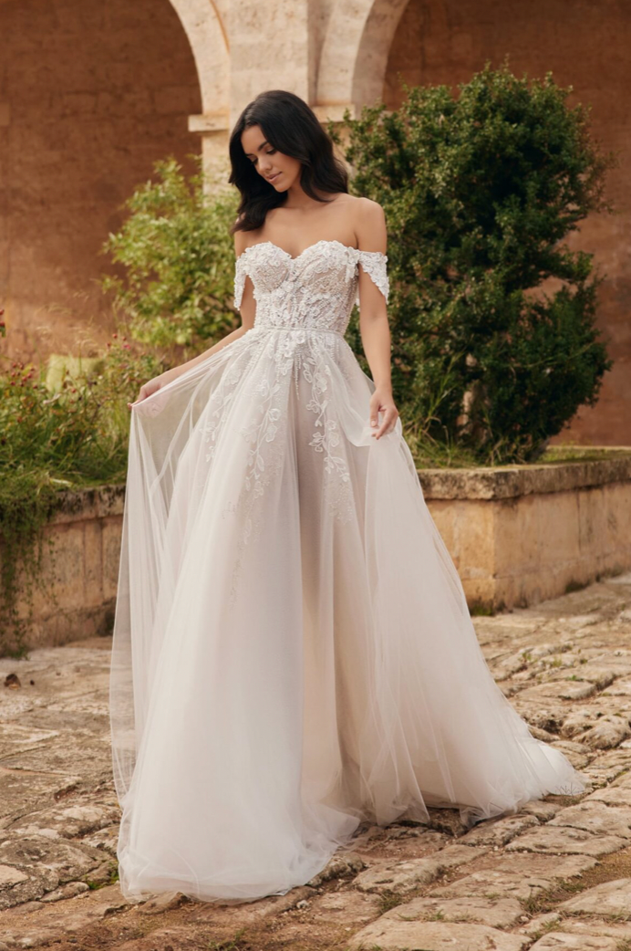 Eine Frau in einem weißen Hochzeitskleid steht vor einer Steinmauer.