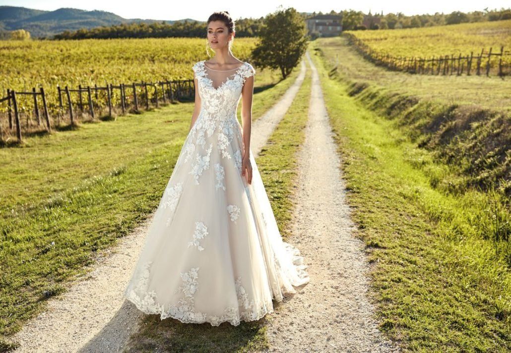 Eine Frau in einem Brautkleid steht auf einem Feldweg.