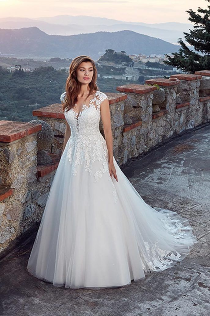 Eine Frau in einem weißen Hochzeitskleid steht vor einer Steinmauer.