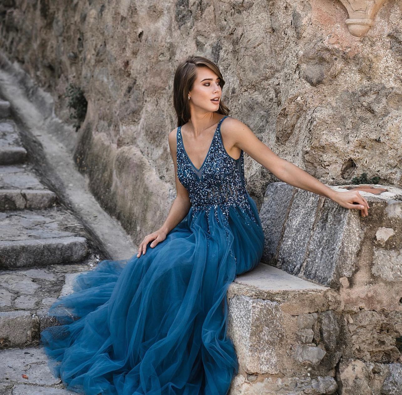 Eine Frau in einem blauen Kleid sitzt auf einer Steinmauer