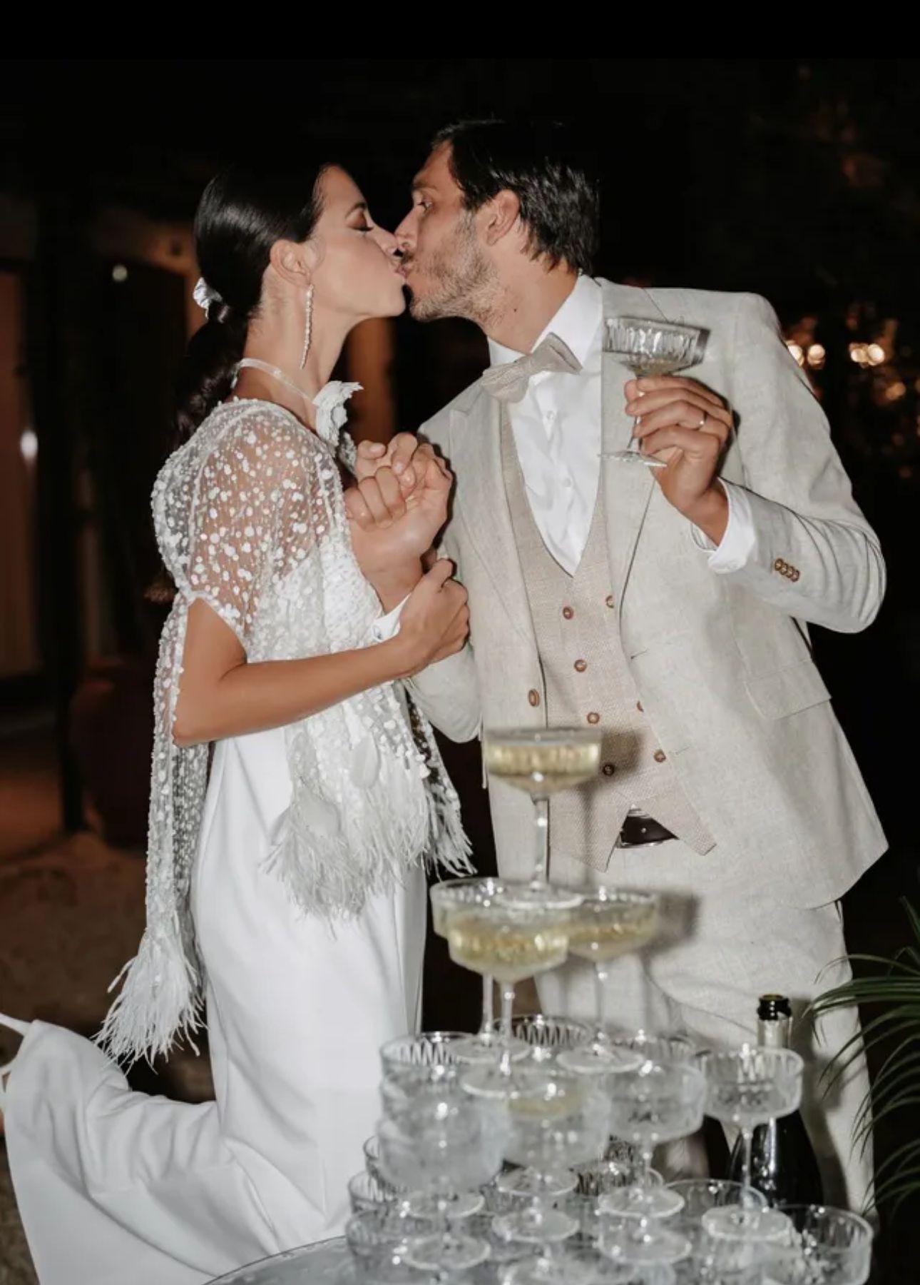 Paar küsst sich bei einer Hochzeit in der Nähe des Champagnerturms; die Braut