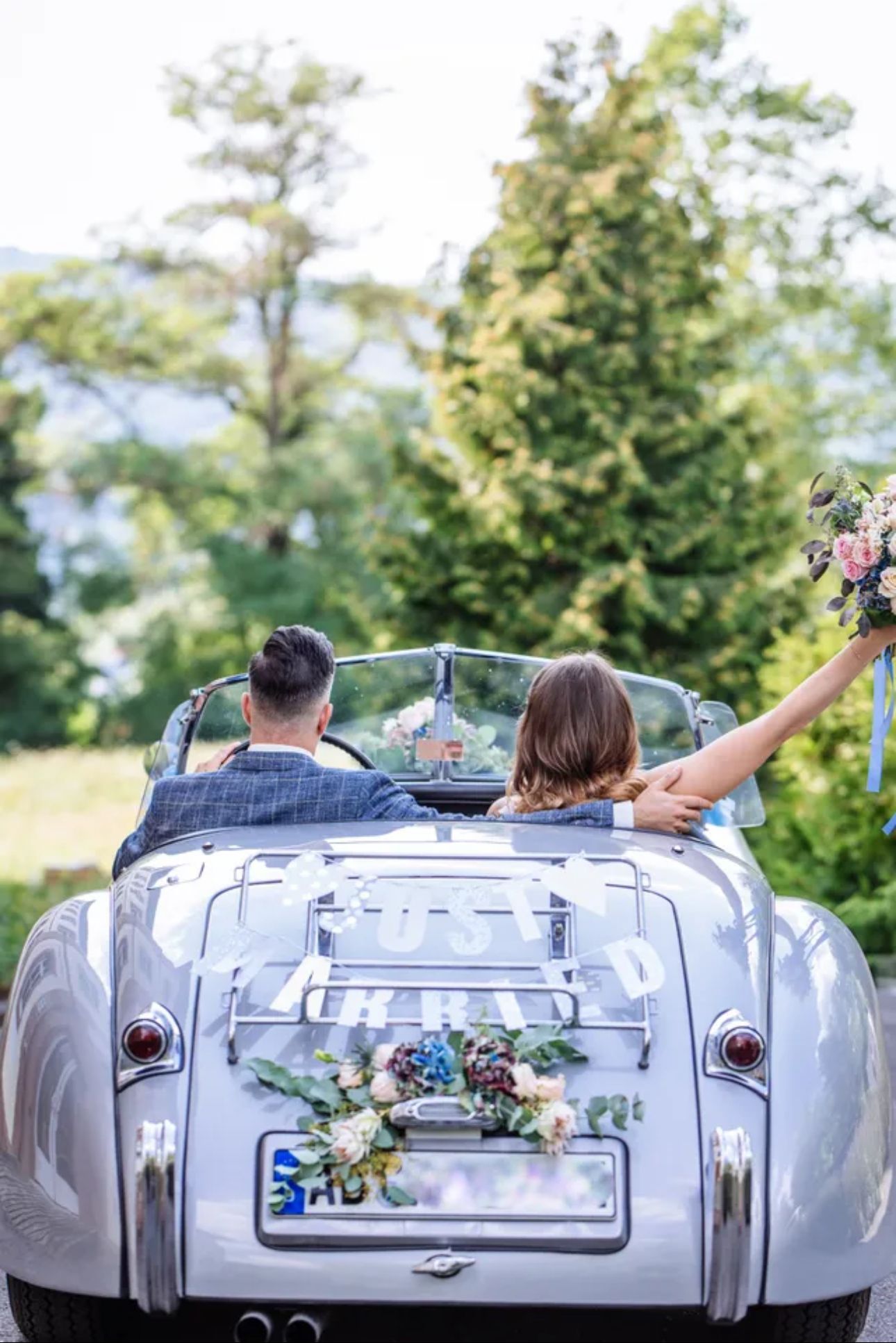 Frischvermählte in einem silbernen Cabrio, „Just Married“-Schild auf der Rückseite