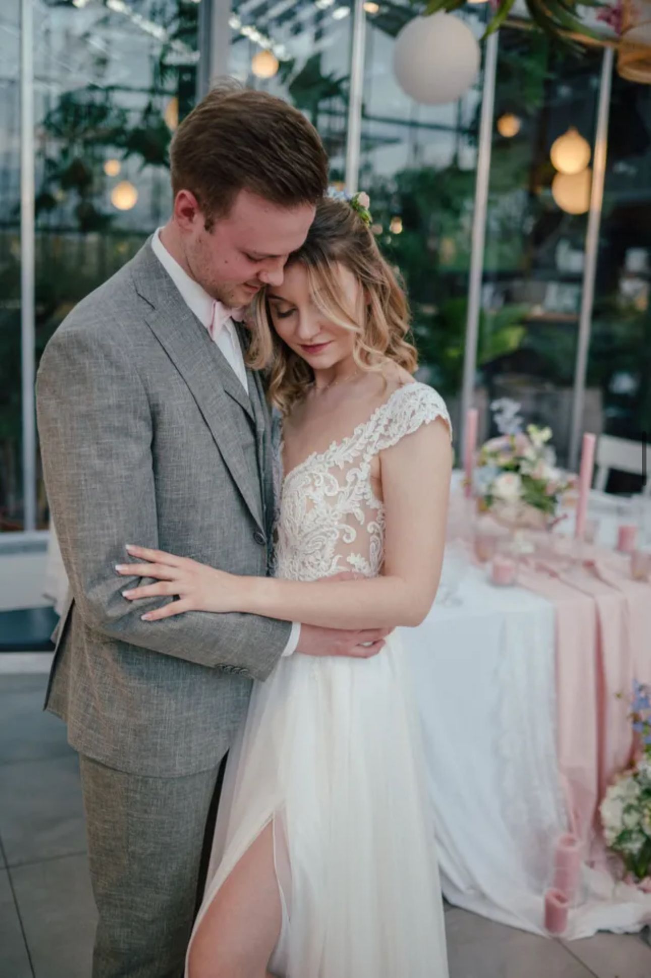 Umarmendes Hochzeitspaar; Mann im grauen Anzug, Frau im weißen Kleid mit transparentem Schlitz; Innenaufnahme.