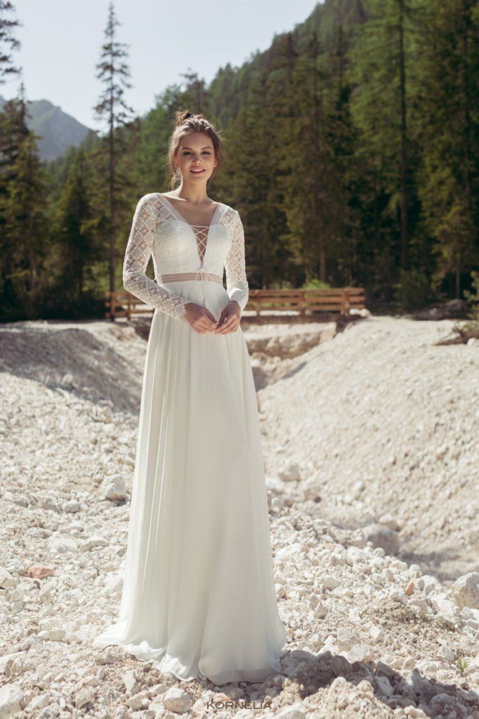 Eine Frau in einem weißen Hochzeitskleid steht an einem steinigen Strand.