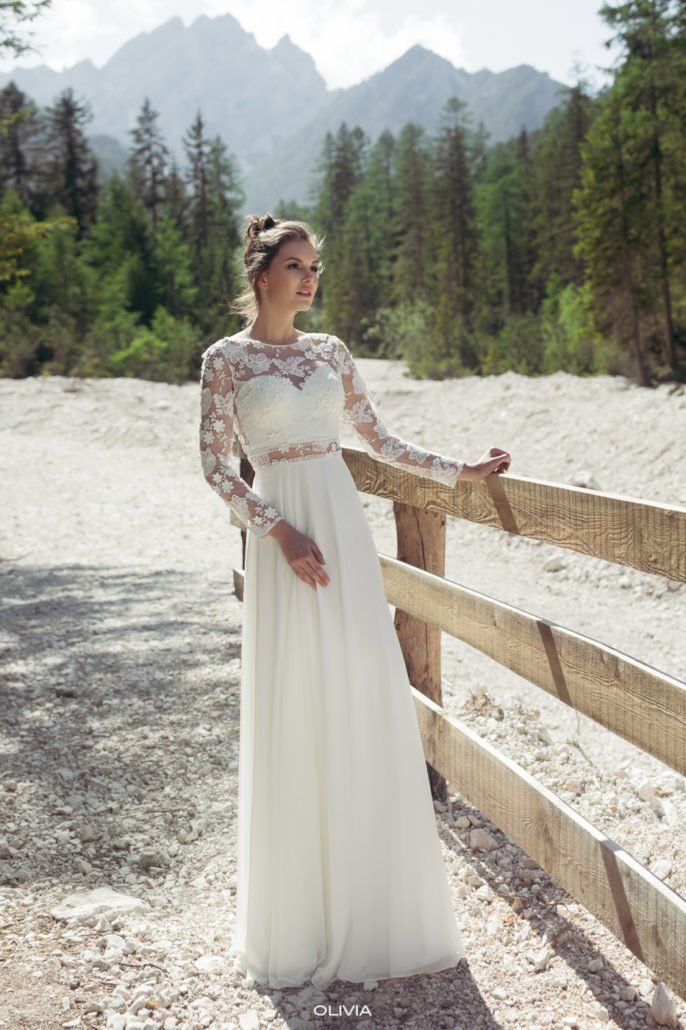Eine Frau in einem Brautkleid steht neben einem Holzzaun.