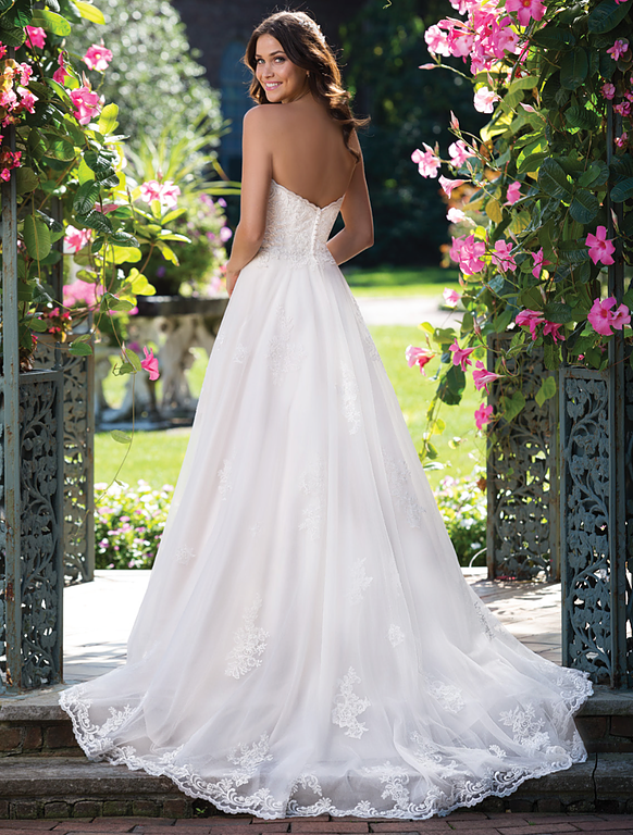 Eine Frau in einem weißen Hochzeitskleid steht vor Blumen.