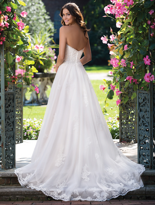Eine Frau in einem weißen Hochzeitskleid steht vor Blumen.