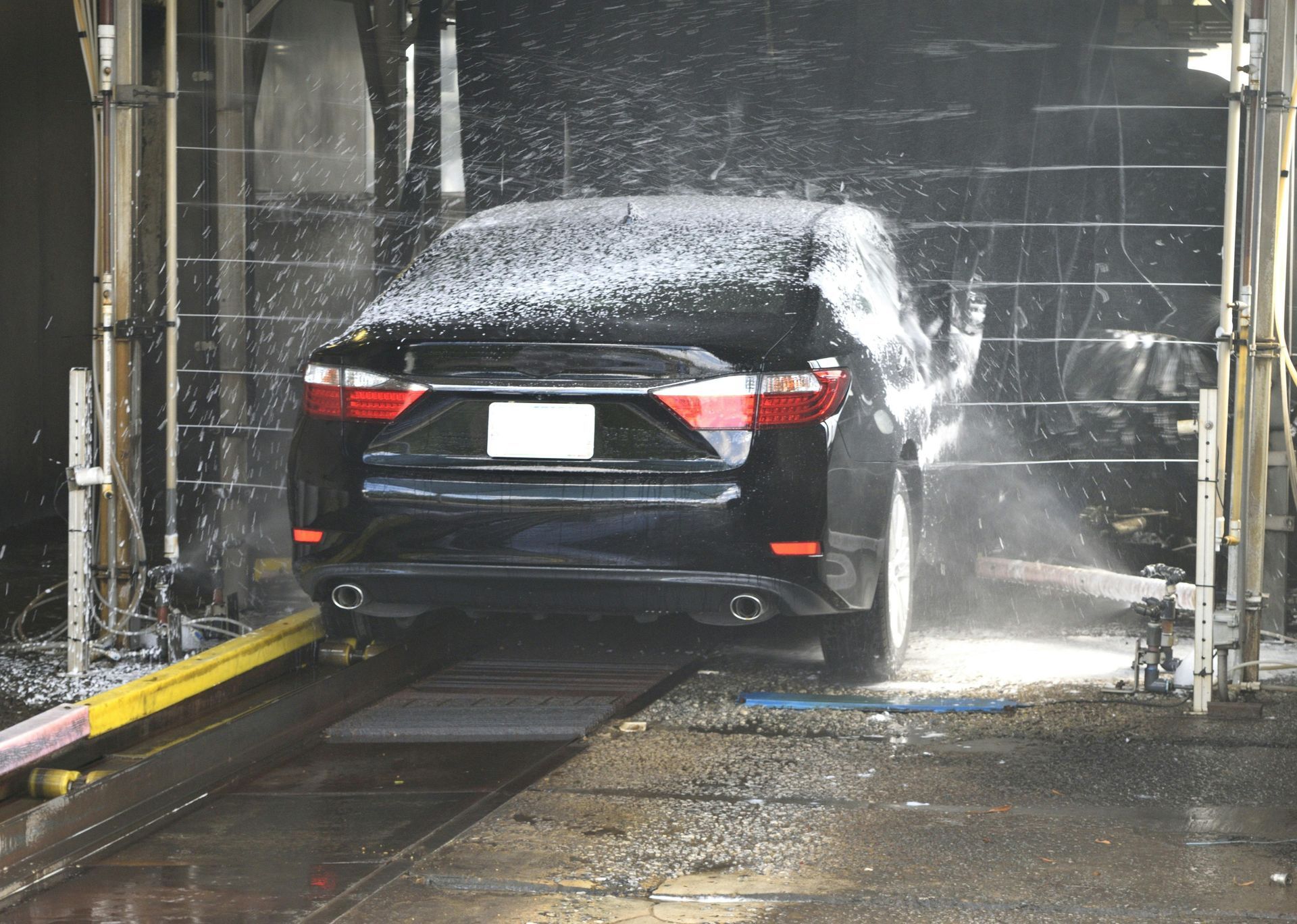 Black car being washed in an automatic car wash. Foamy soap covers the car.