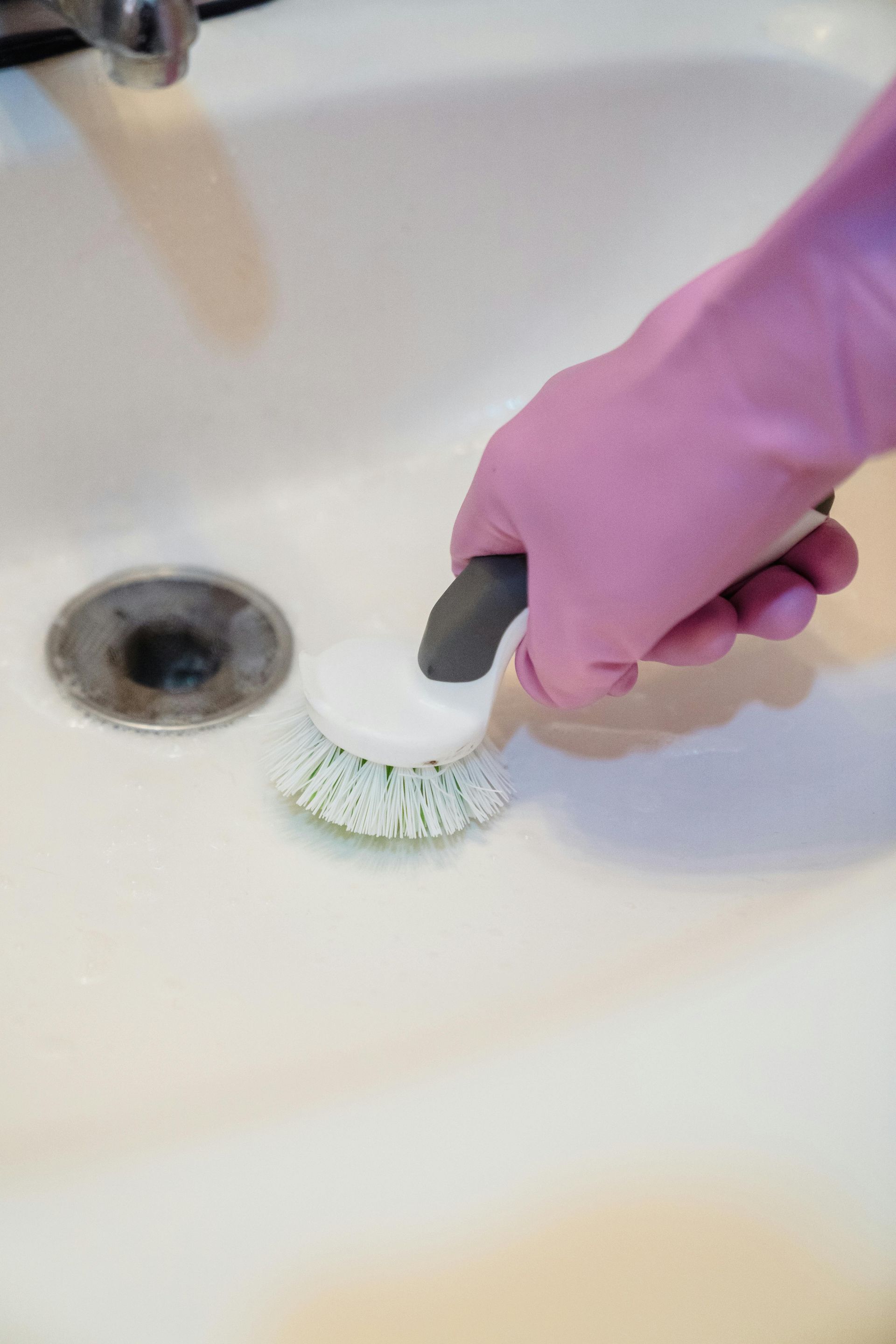 Person wearing a pink glove scrubbing a white sink with a brush.