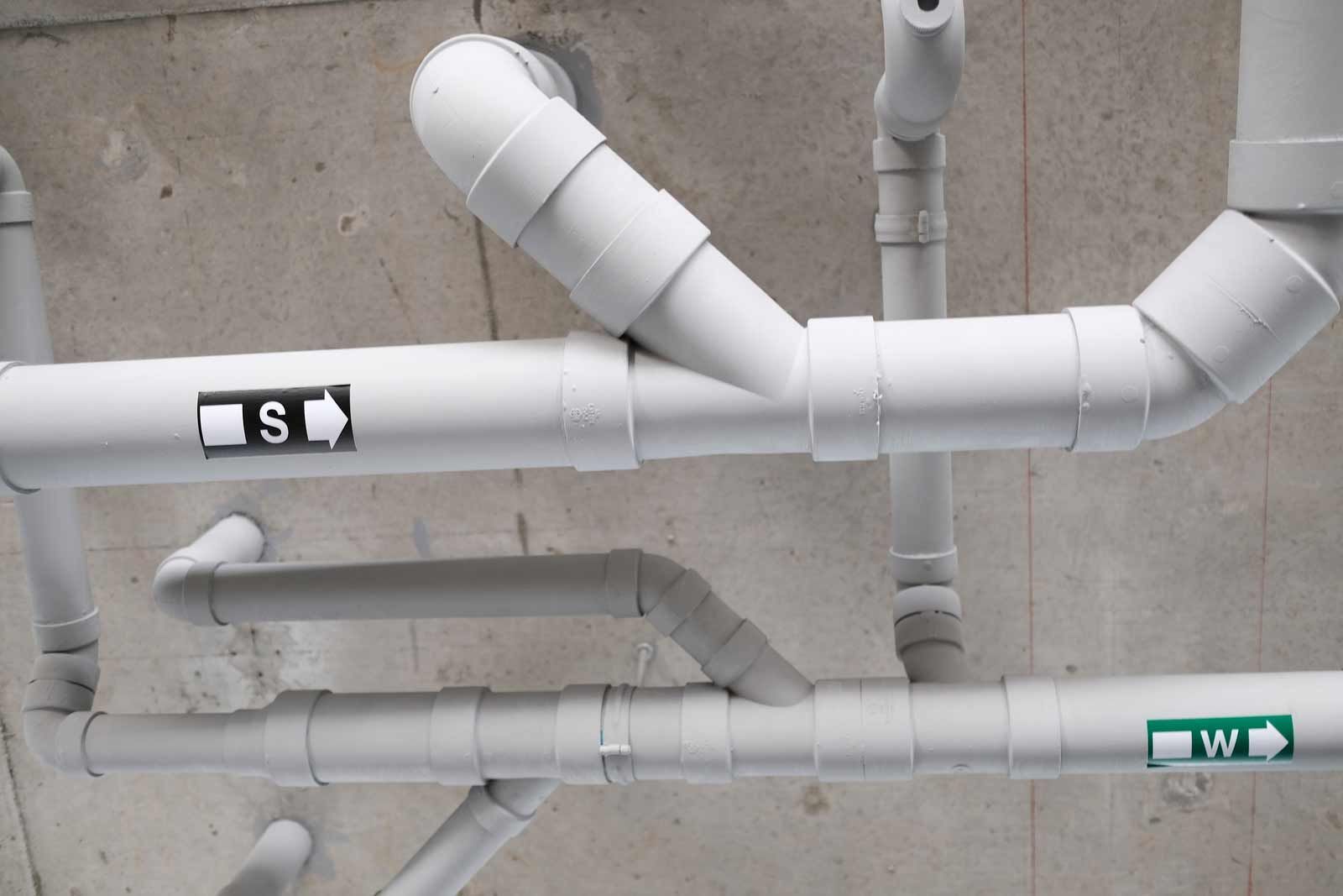White pipes with labeled sections run across a concrete ceiling.