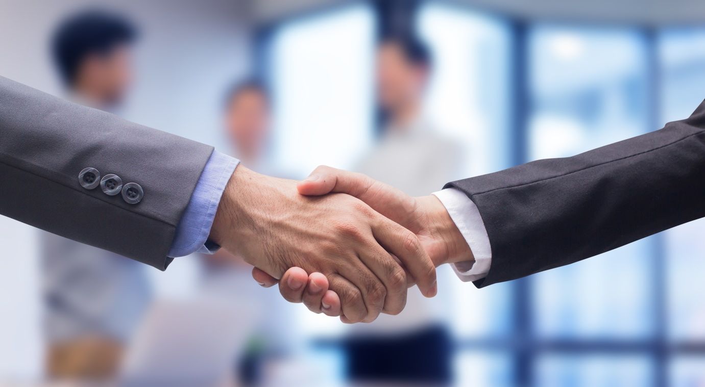 Two business professionals wearing dress shirts and blazers shake hands.