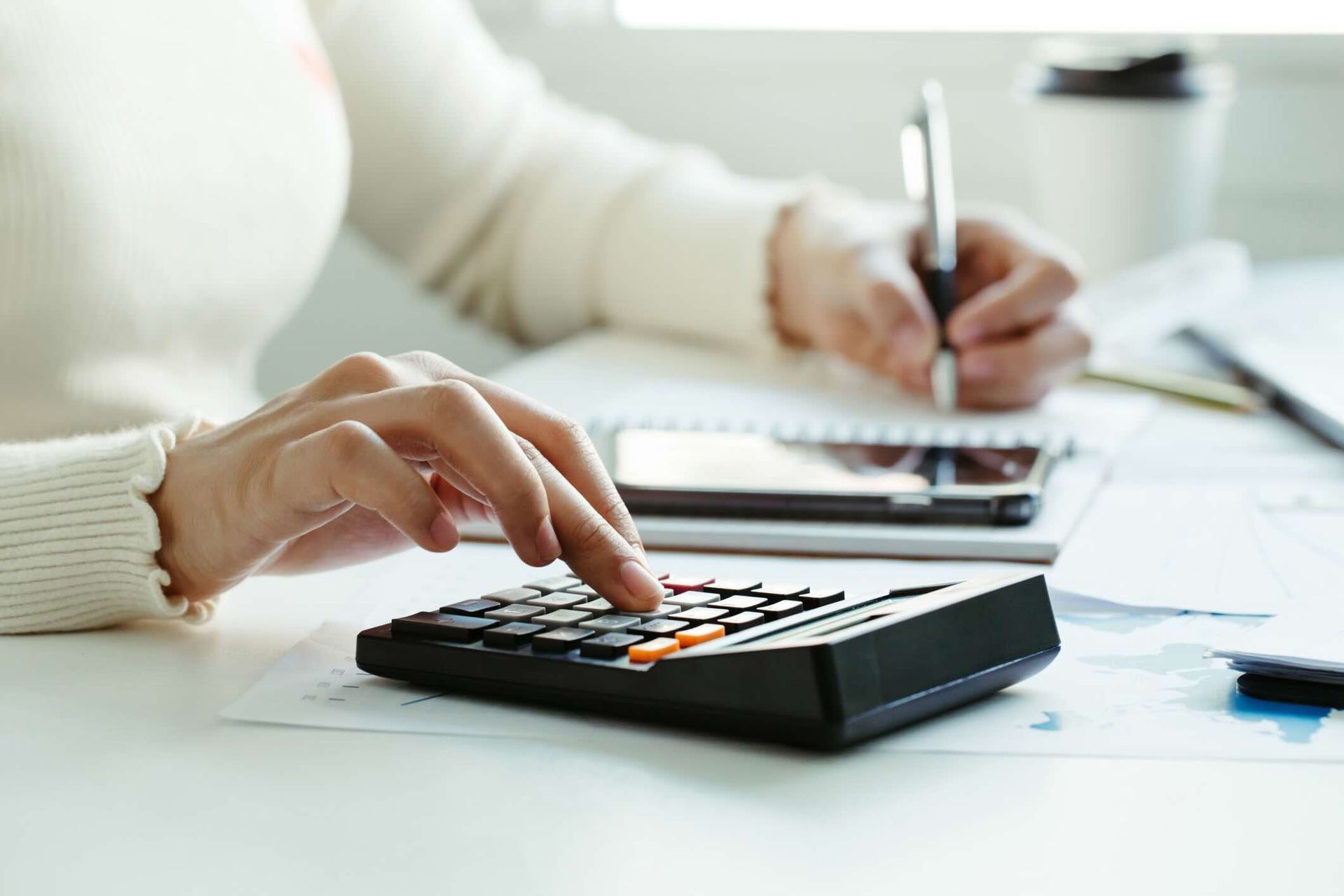 Woman hand using calculator and writing make note with calculate about cost at home office.