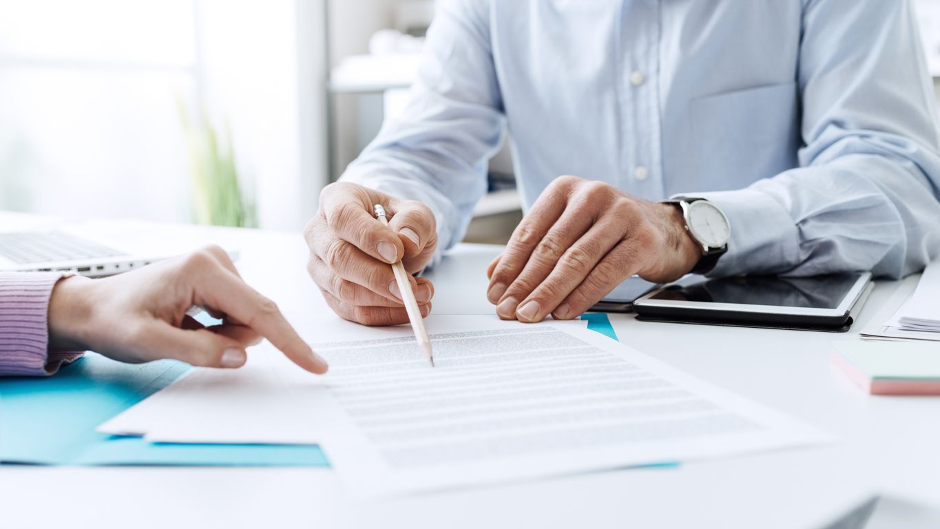 A man wearing a blue business shirt reviews a contract with a white pencil.