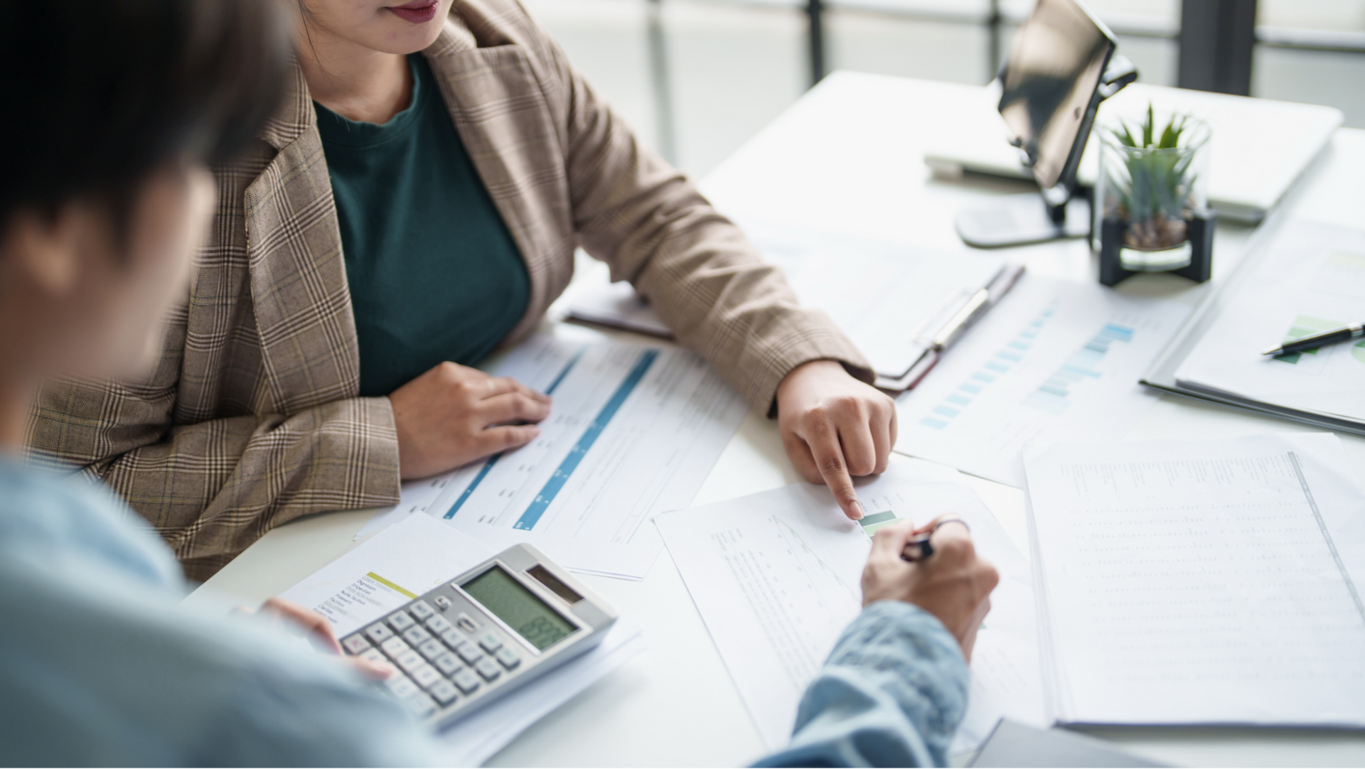 Two people sitting at a table with a calculator and pointing at papers.