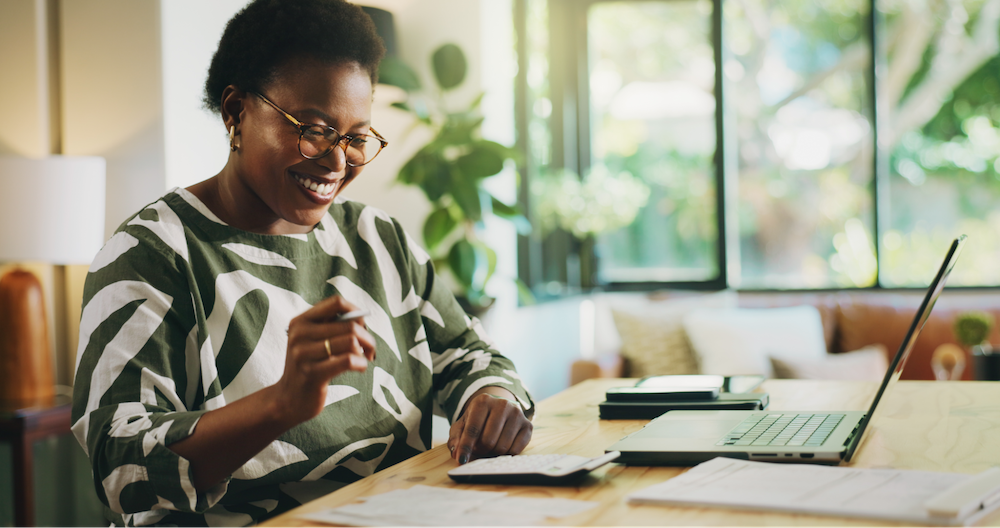 Woman smiling while sitting down at desk and using a calculator