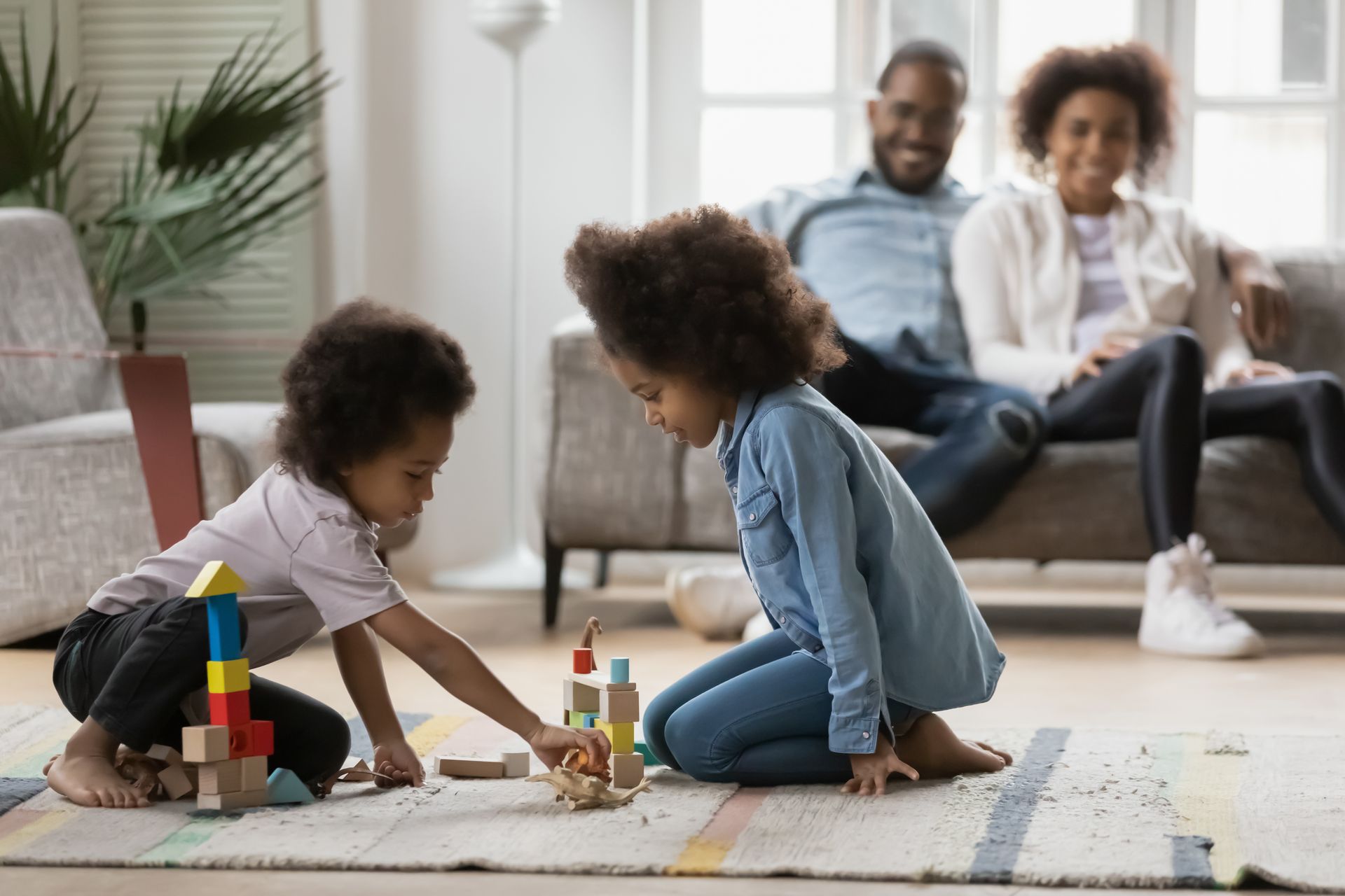 parents sit on the couch in the back discussing self-insured and fully-insured plans for their family