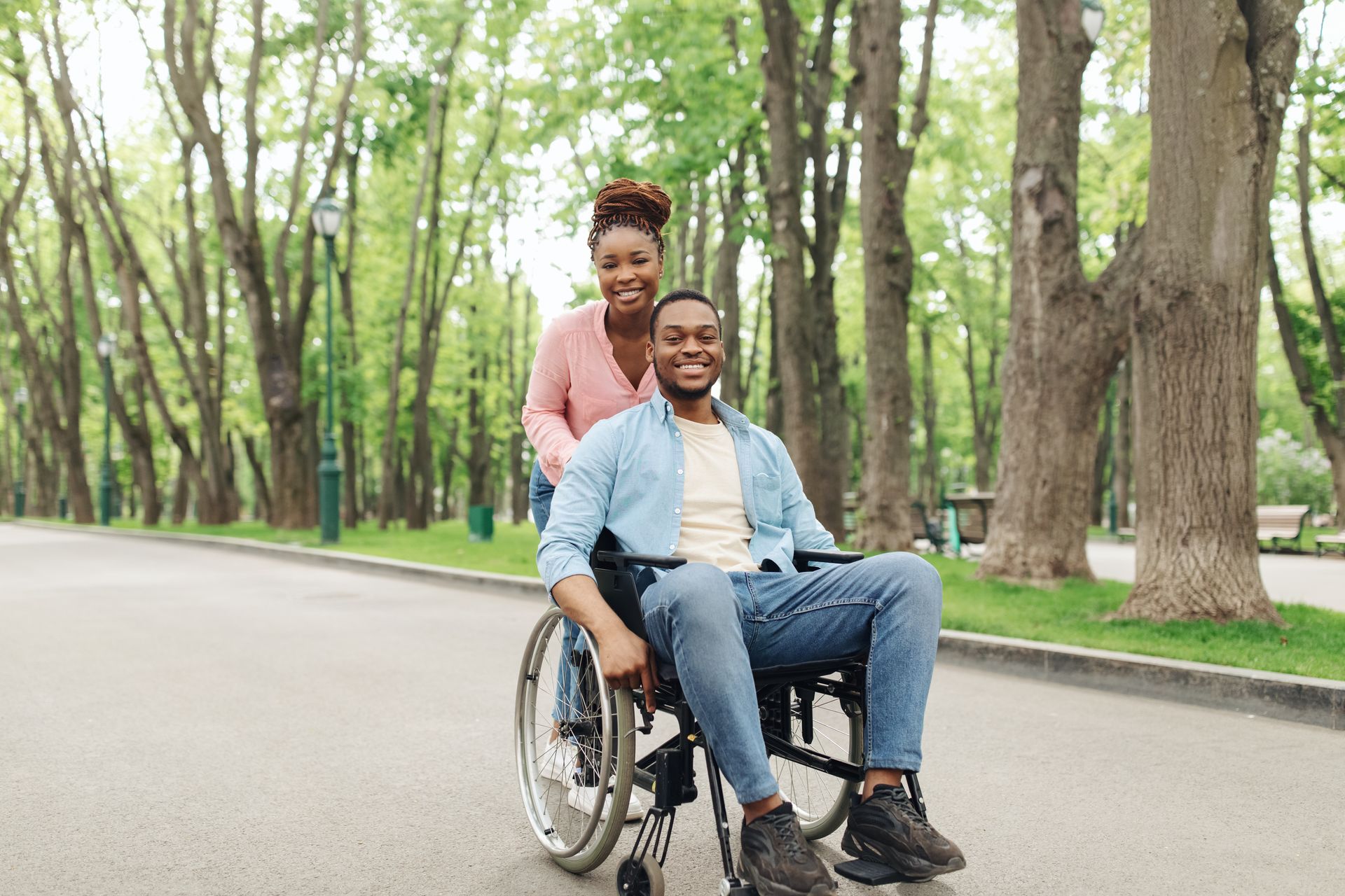 the man in a wheel chair is pushed by a woman in a park, he now understands the difference between workers comp vs disability