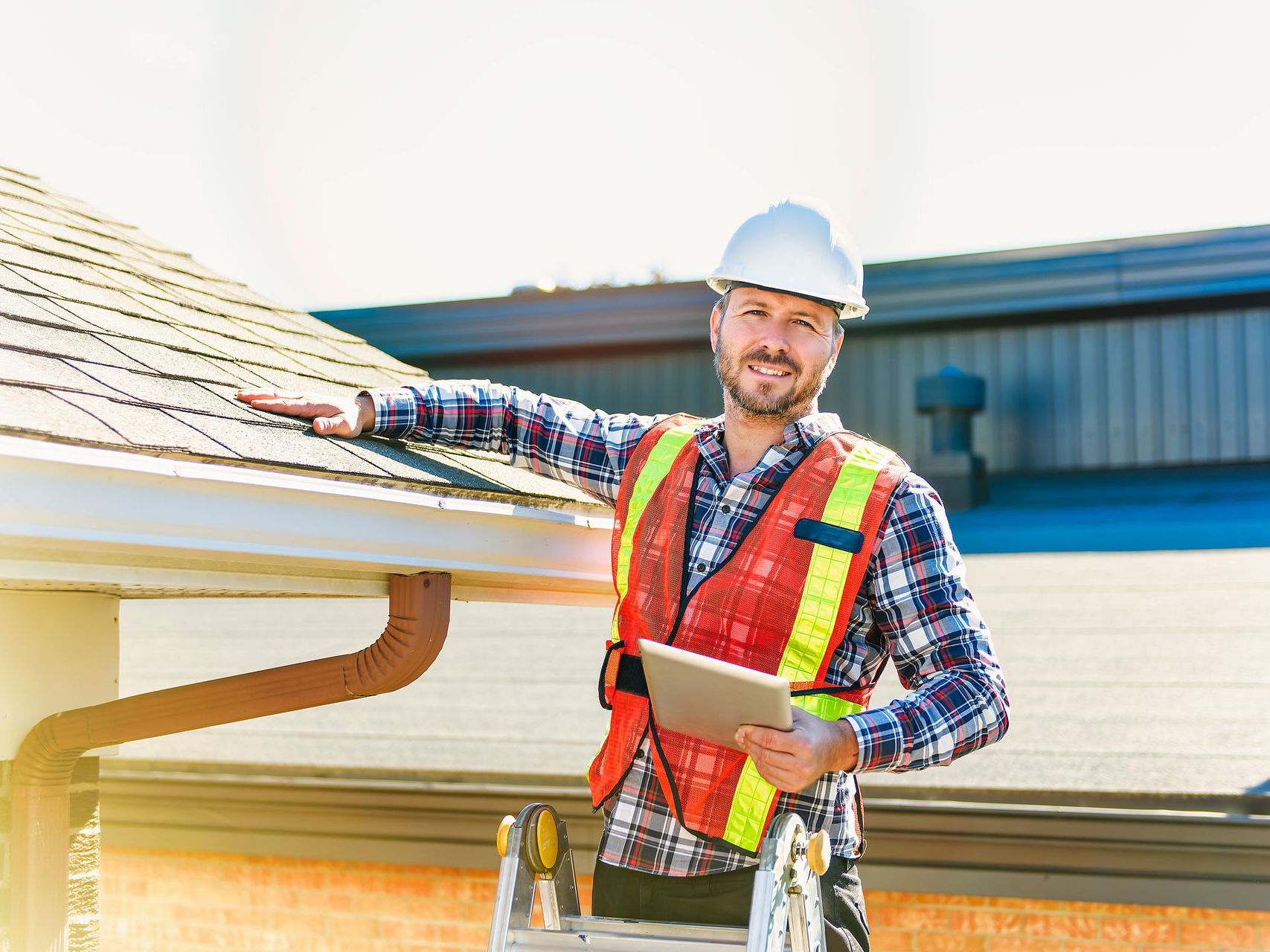 Roofer, protected by roofing business insurance, standing on a ladder doing a final inspection