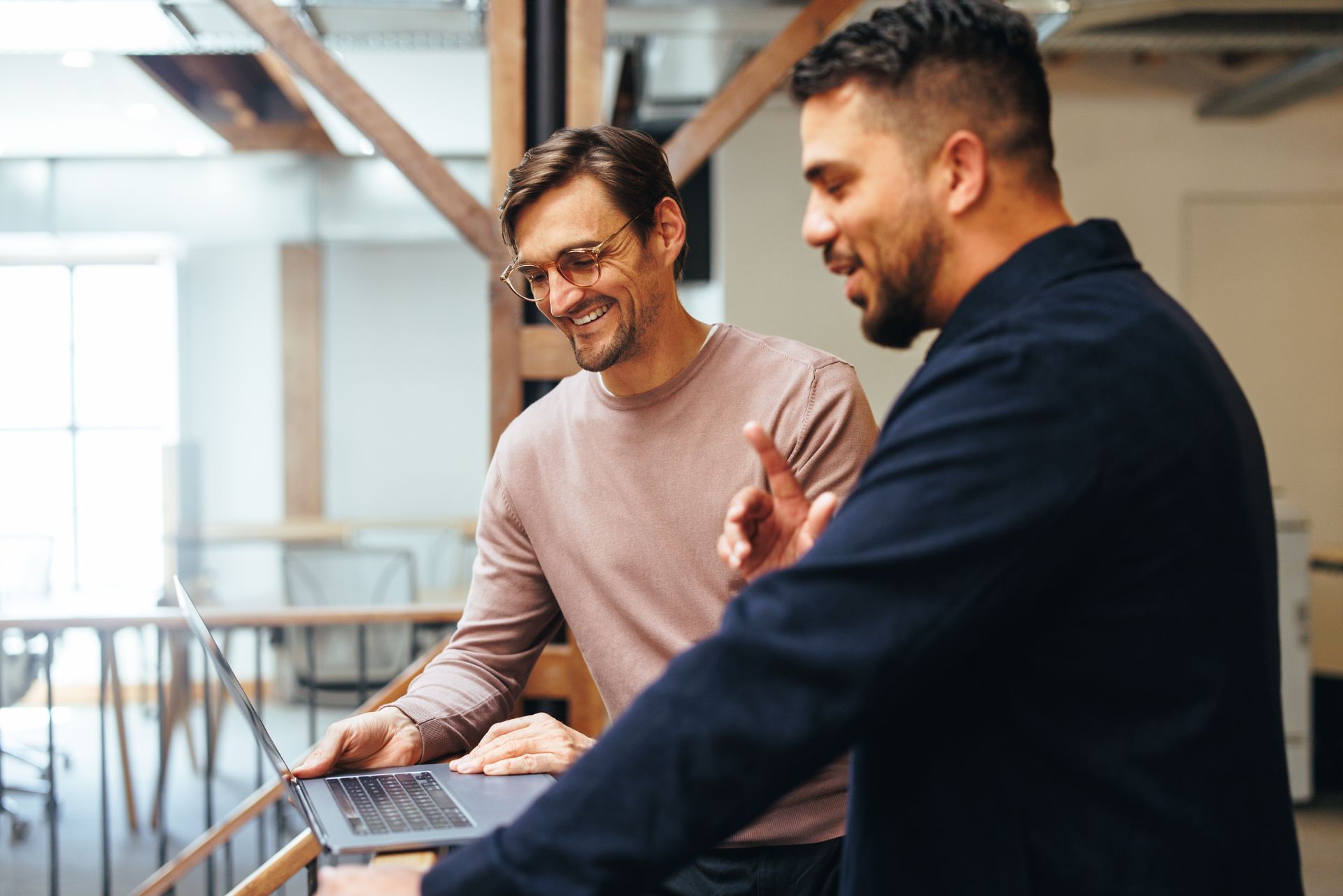 two men are looking at a laptop together and smiling discussing directors and officers liability insurance