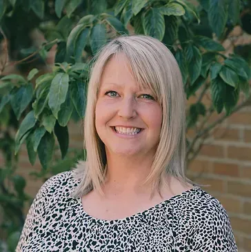 A woman in a leopard print shirt is smiling in front of a tree.