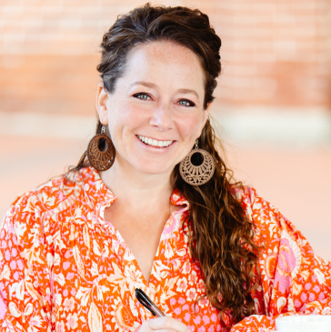 A woman in a leopard print shirt is smiling in front of a tree.
