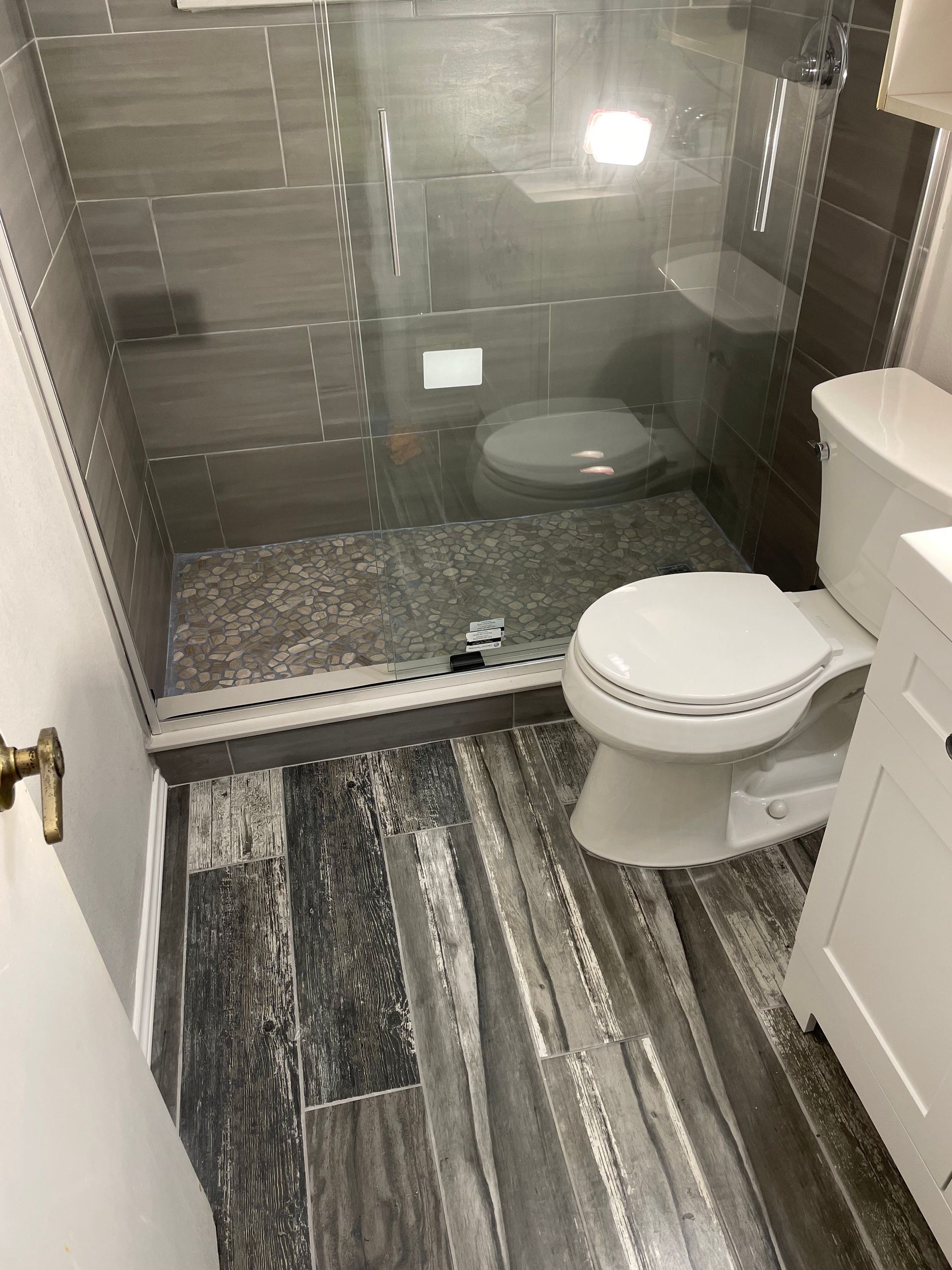 Small bathroom with striped floor, glass shower, and toilet in the foreground.