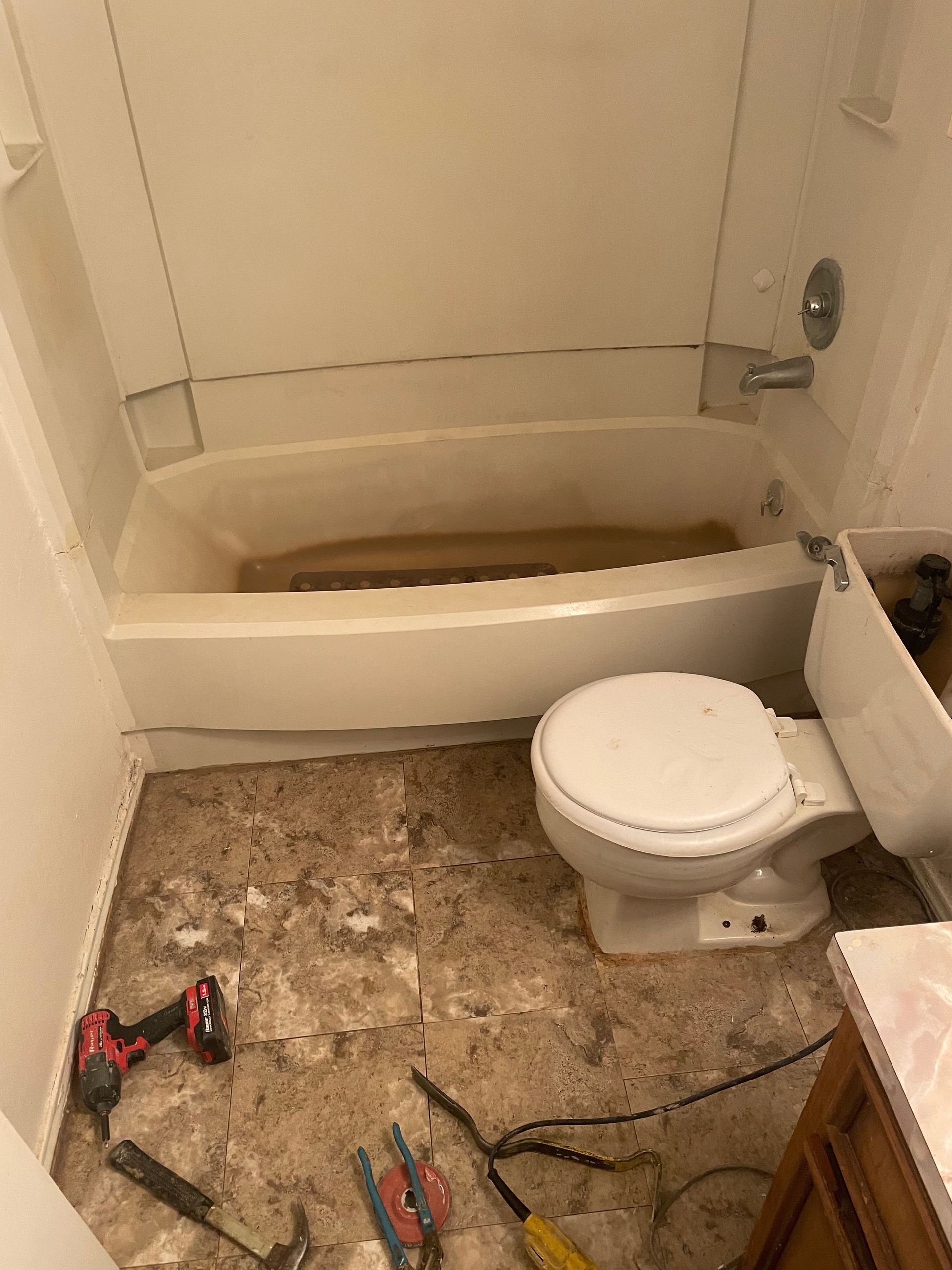 Small bathroom under renovation with a white tub, toilet, and tools on the floor.