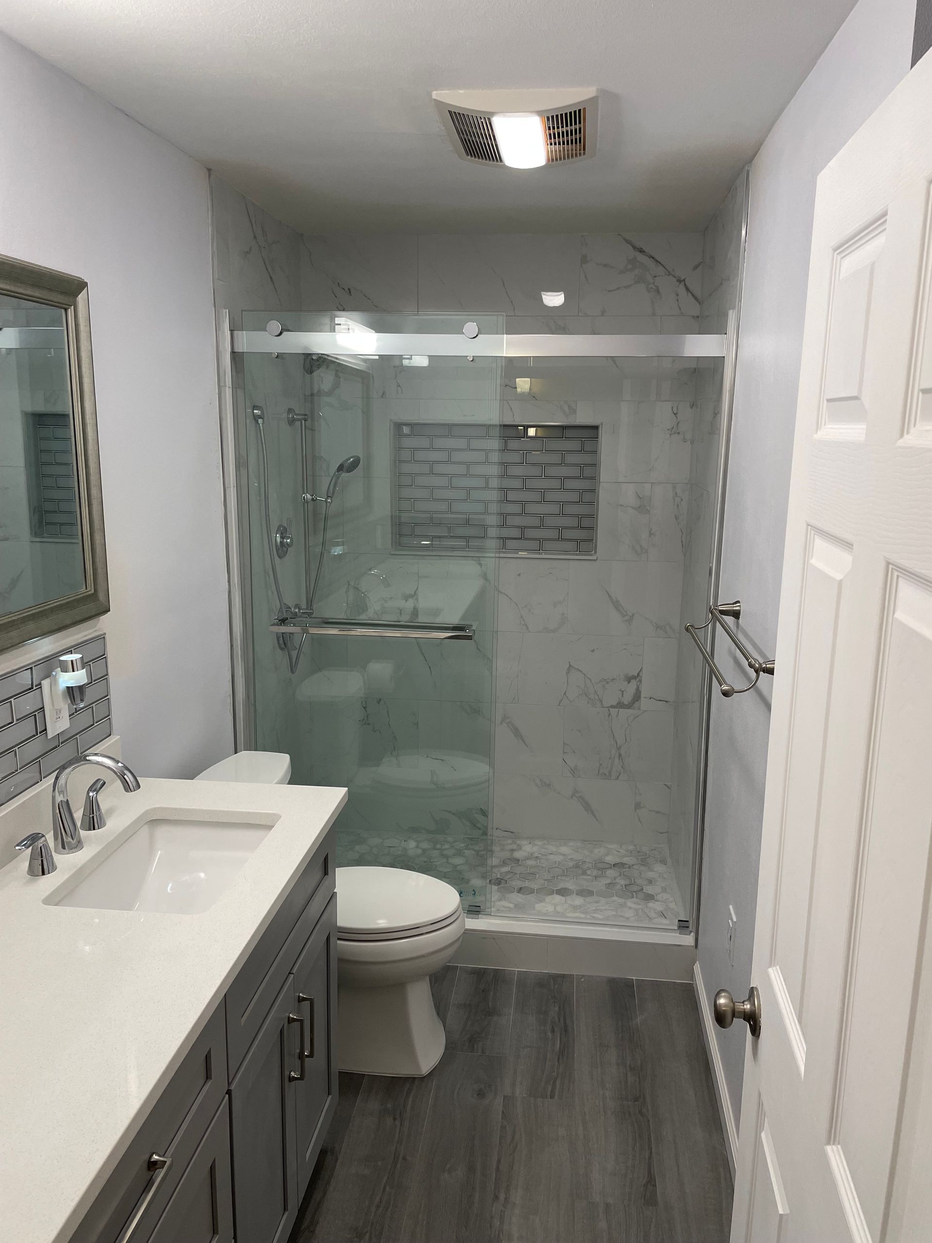 Modern bathroom with glass shower, vanity sink, toilet, and gray wood-look floor.