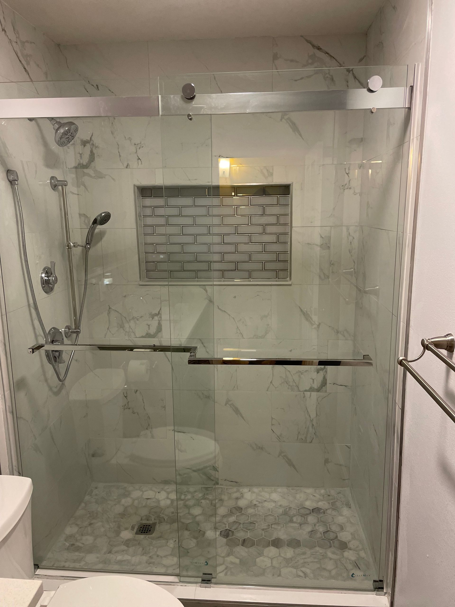 Glass shower with tiled niche, chrome fixtures, and white bathroom walls.