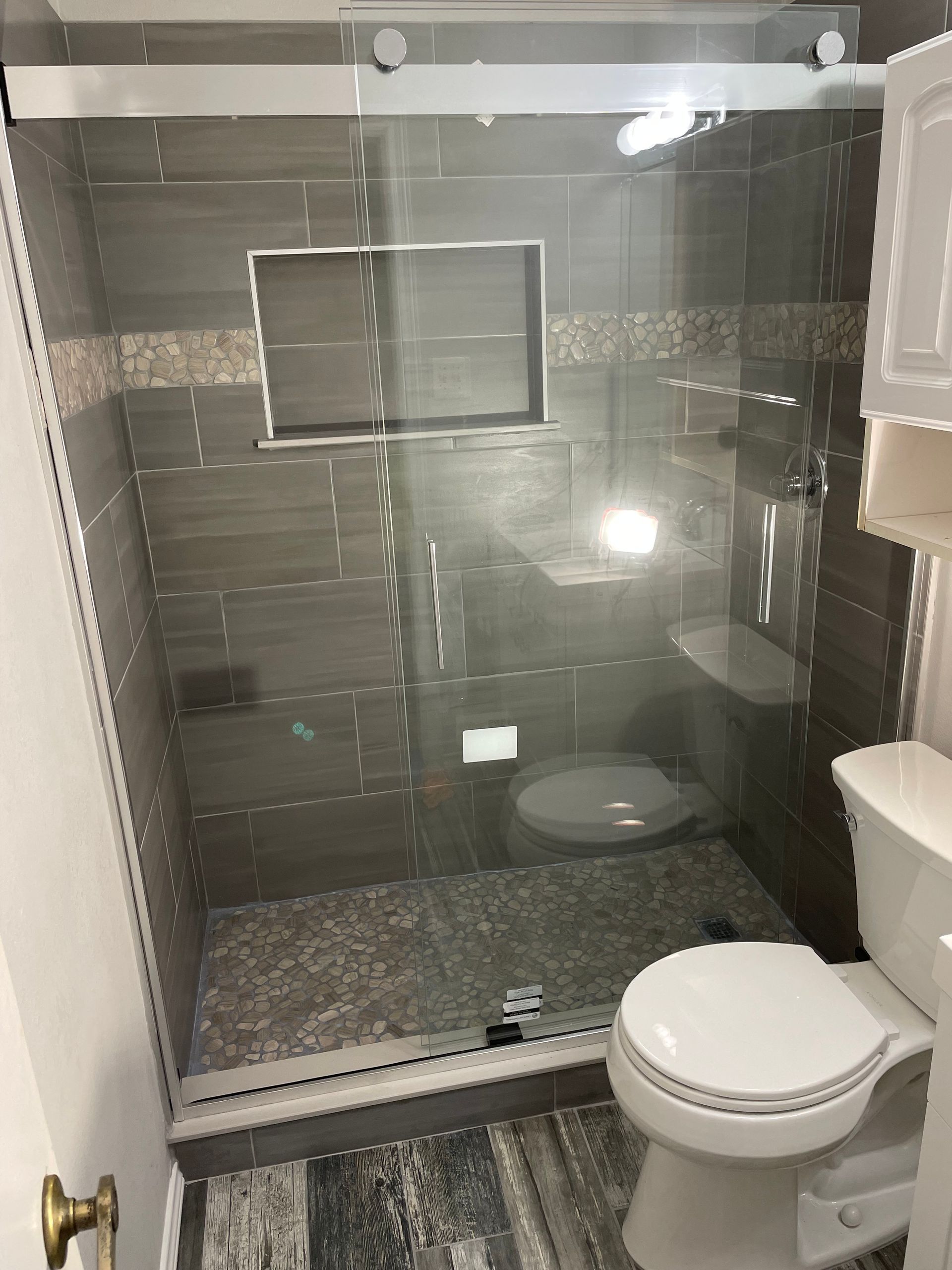 Small bathroom with a glass walk-in shower, toilet, and vanity sink, viewed from the doorway.