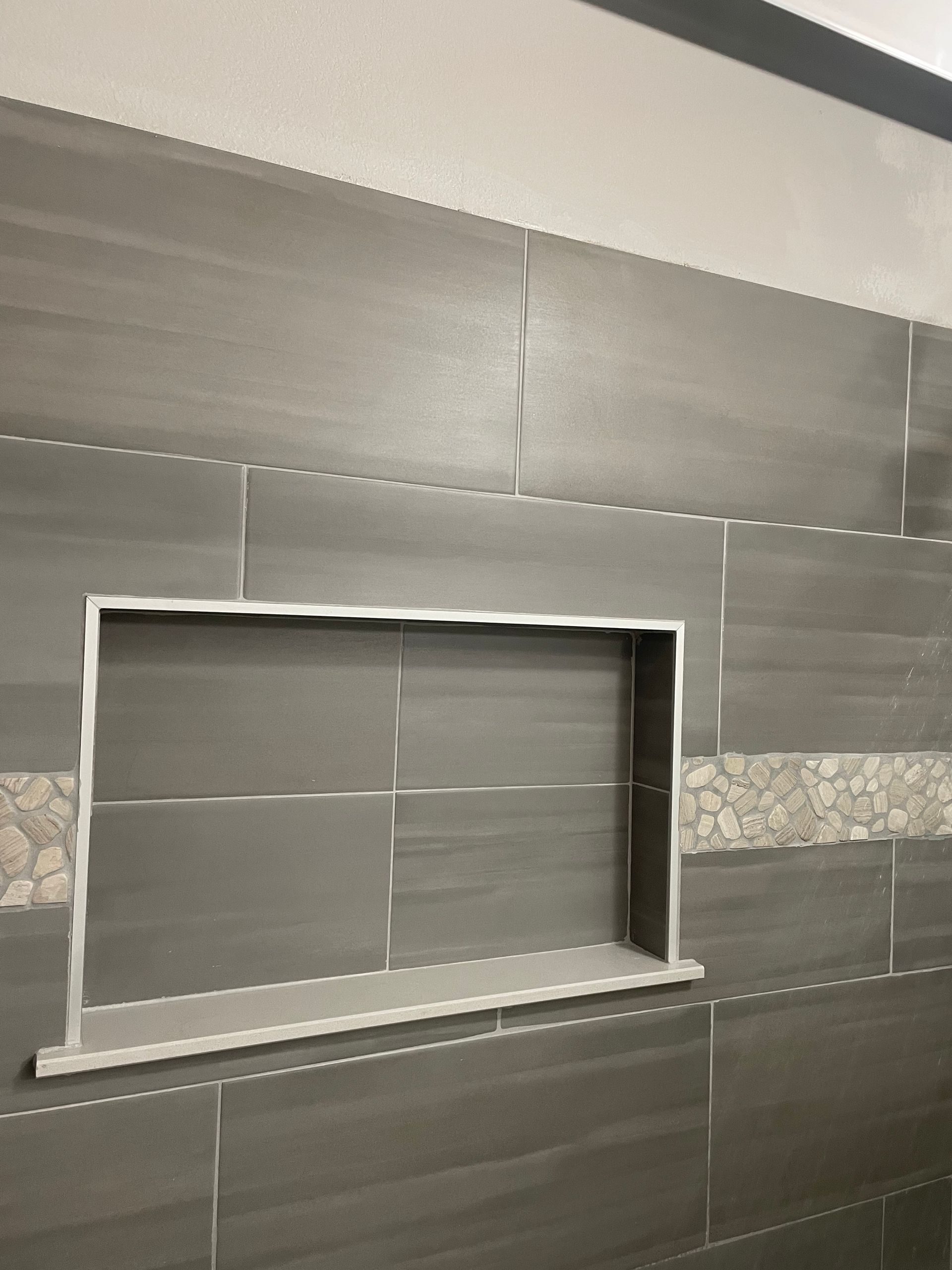 Tiled wall with a recessed rectangular niche and a strip of decorative stone tile running horizontally.