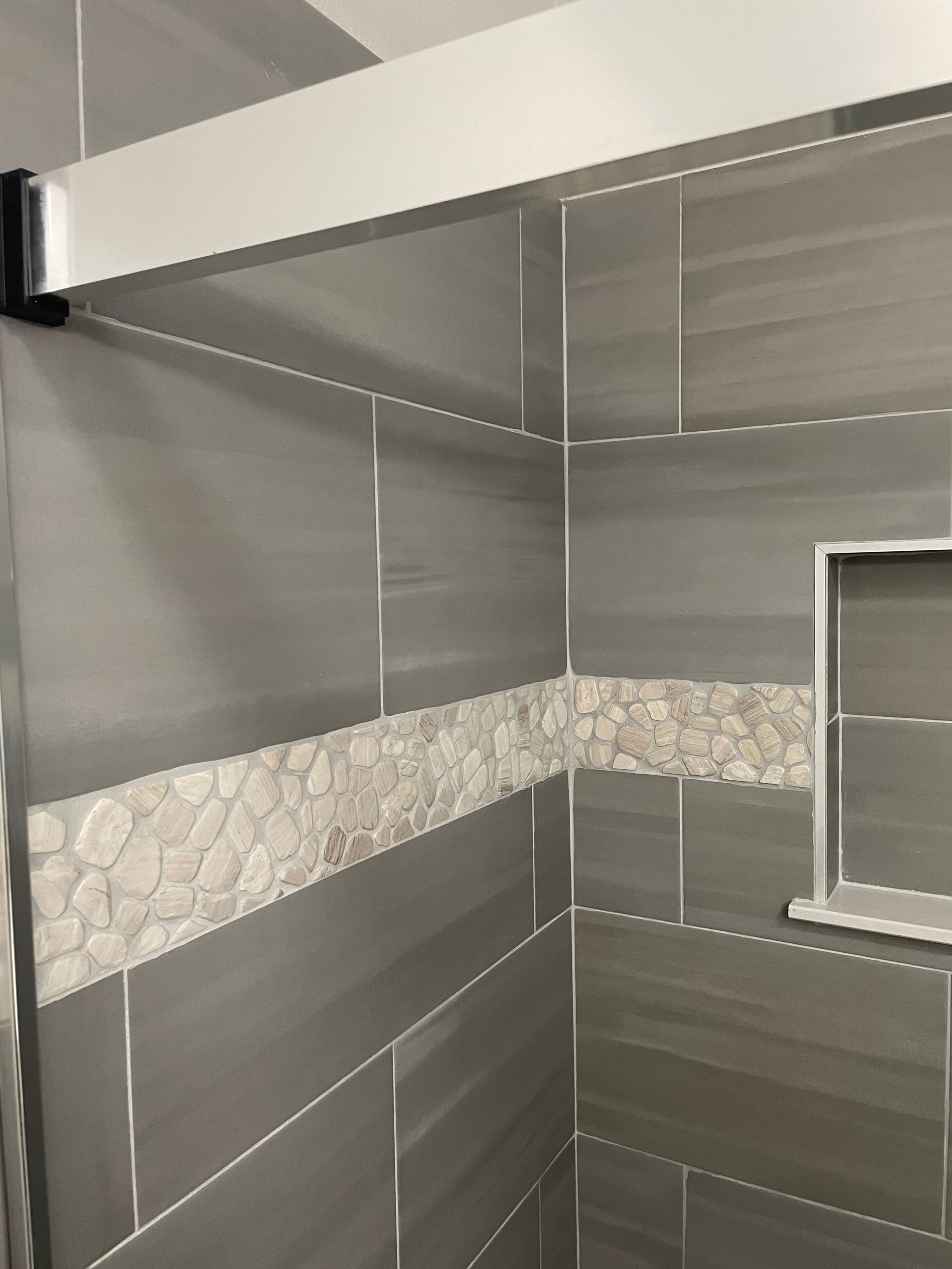 Modern tiled bathroom corner with gray walls, stone accent strip, and a small window