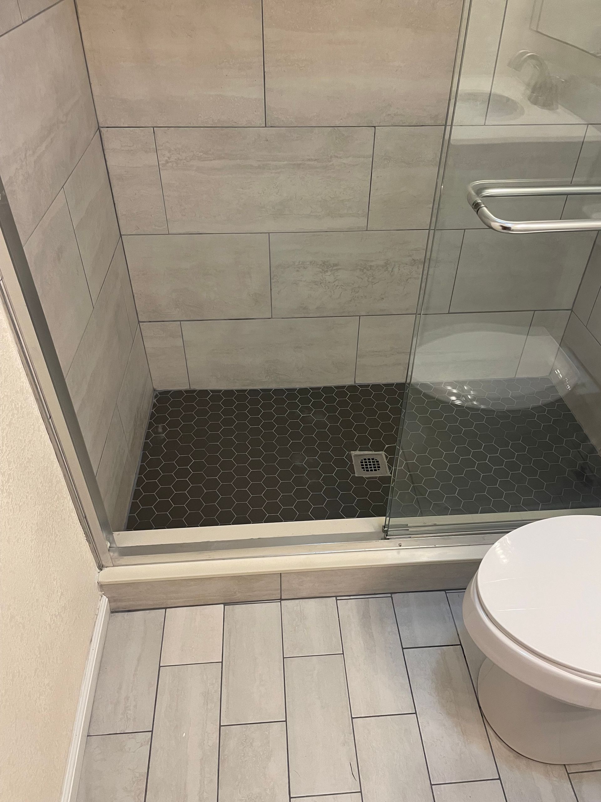 Bathroom with tiled walk-in shower, glass door, dark shower floor, and toilet in foreground