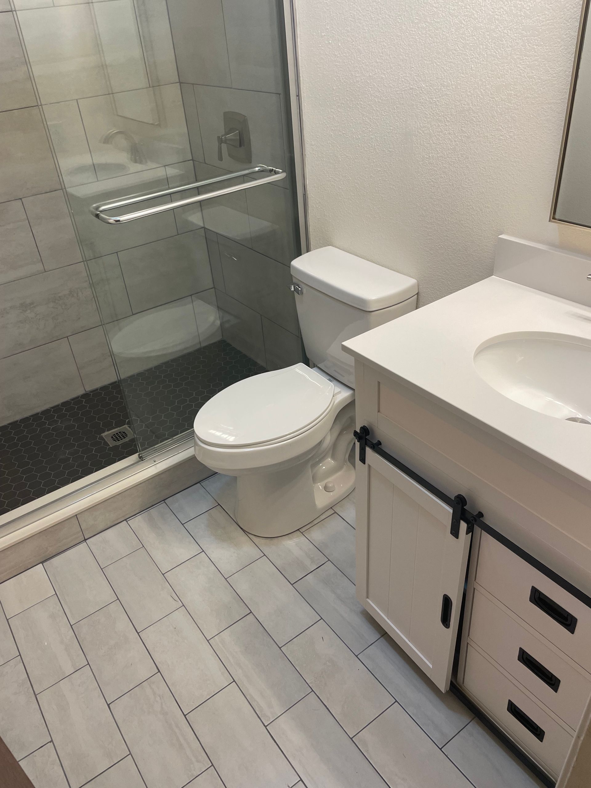 Small bathroom with toilet, glass shower, and white vanity with sink and drawers.