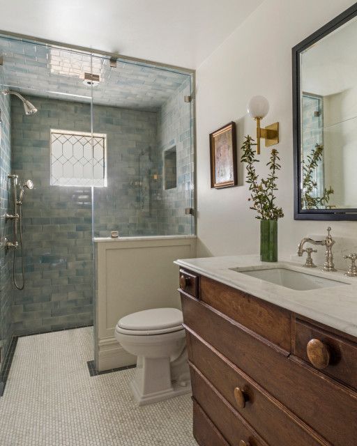 Bright bathroom with glass shower, white tile floor, and wooden vanity with sink and mirror