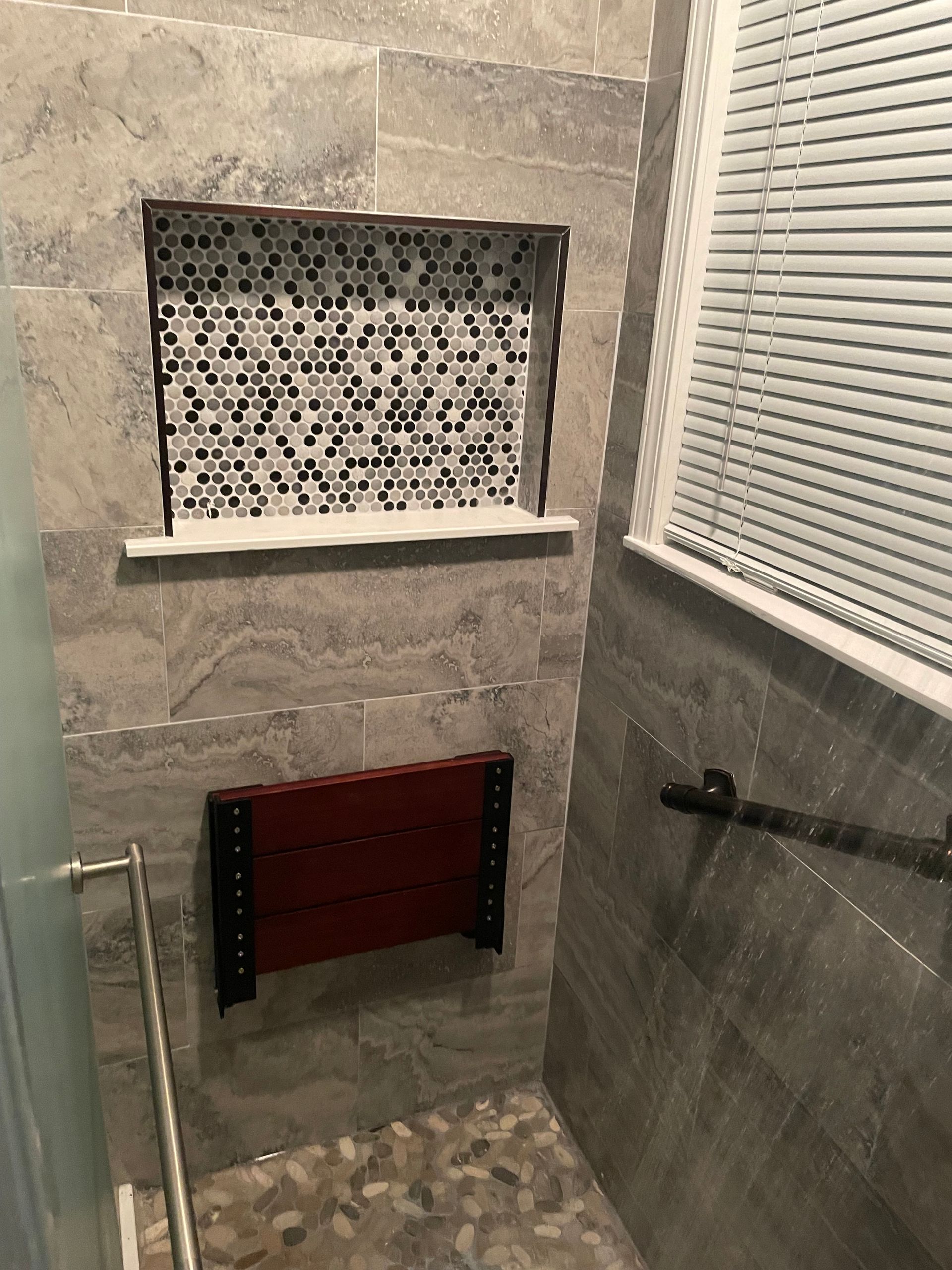Small tiled shower nook with a mosaic shelf, red bench, and glass wall.